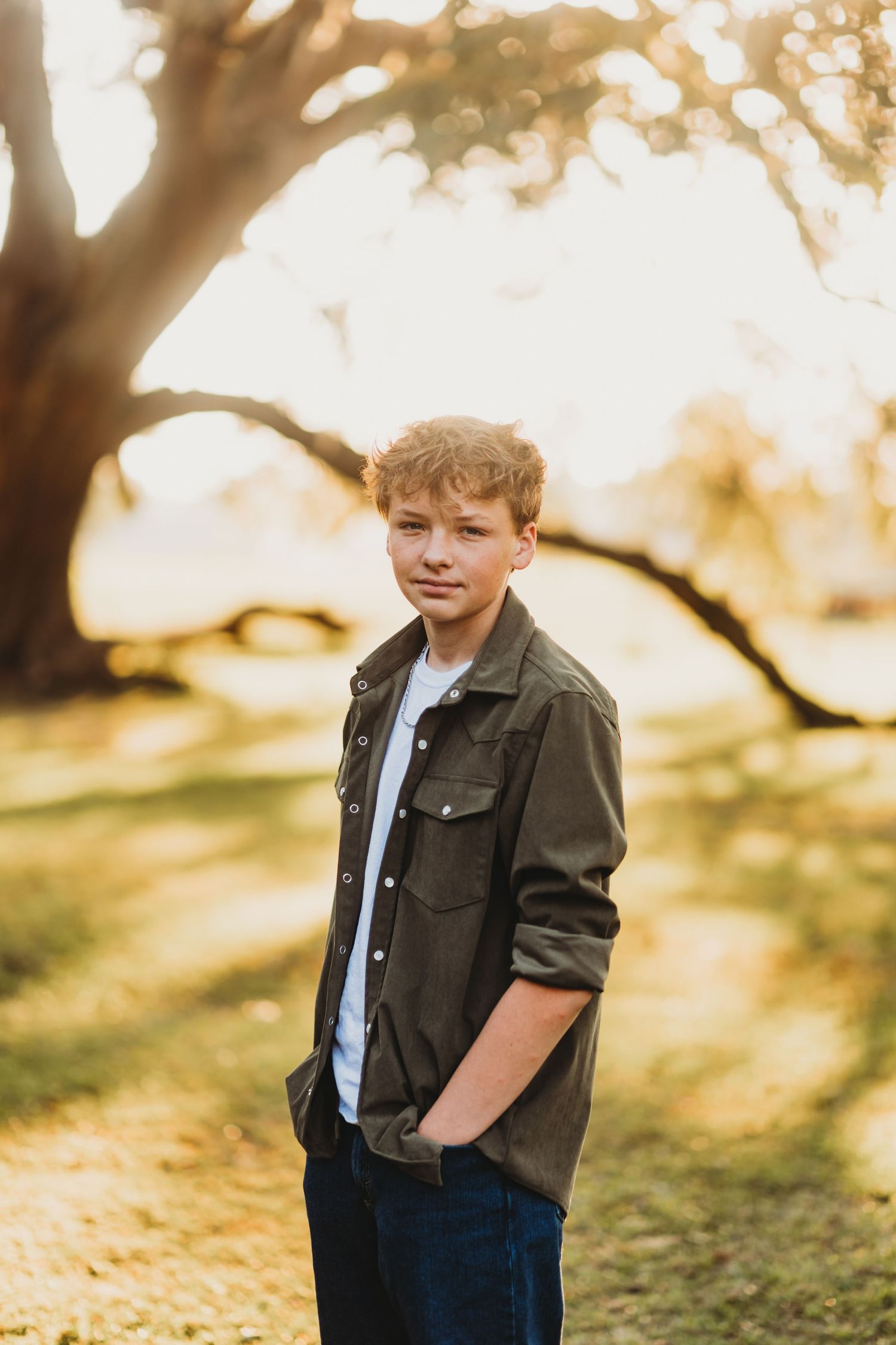 Child wearing brown jacket and jeans poses outdoors in warm sunlight during golden hour photo session.