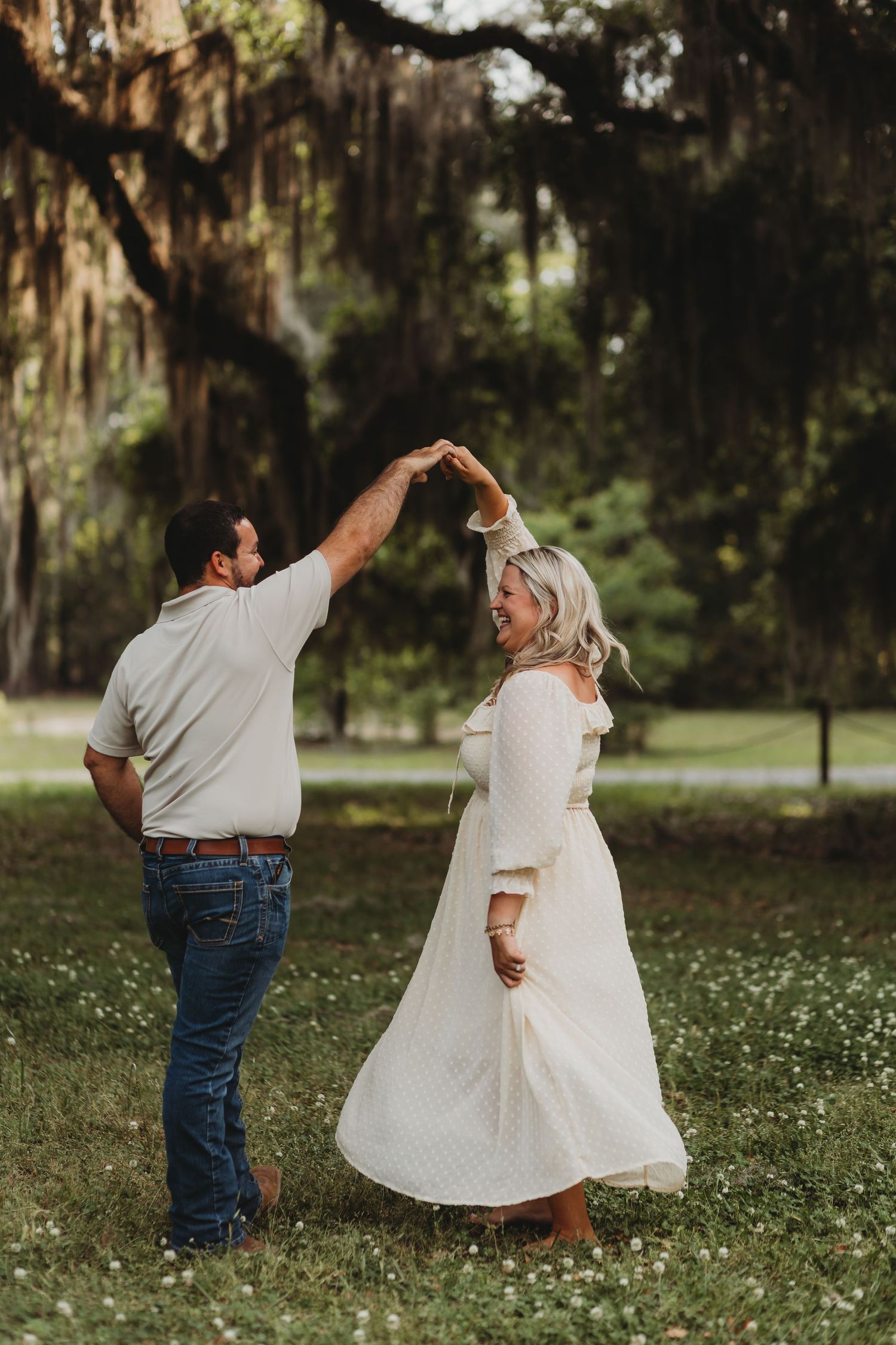 Couple shares a romantic dance moment in a scenic park with Spanish moss trees.