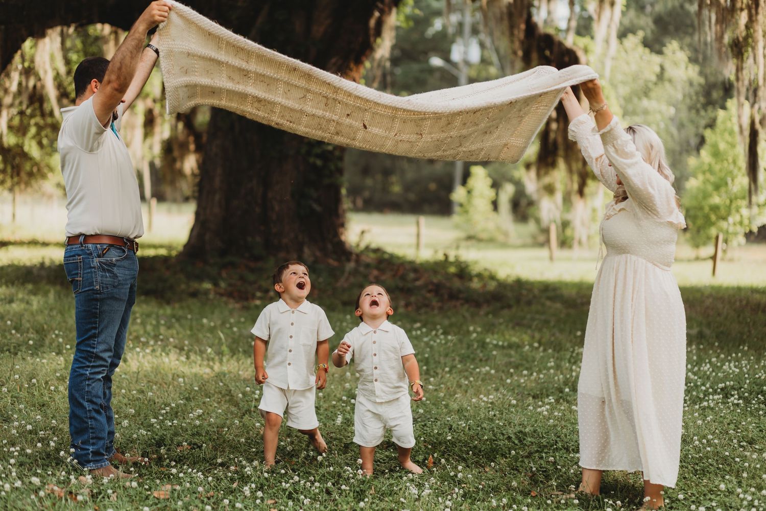 Family holds white blanket in sunlit meadow during outdoor photo session.