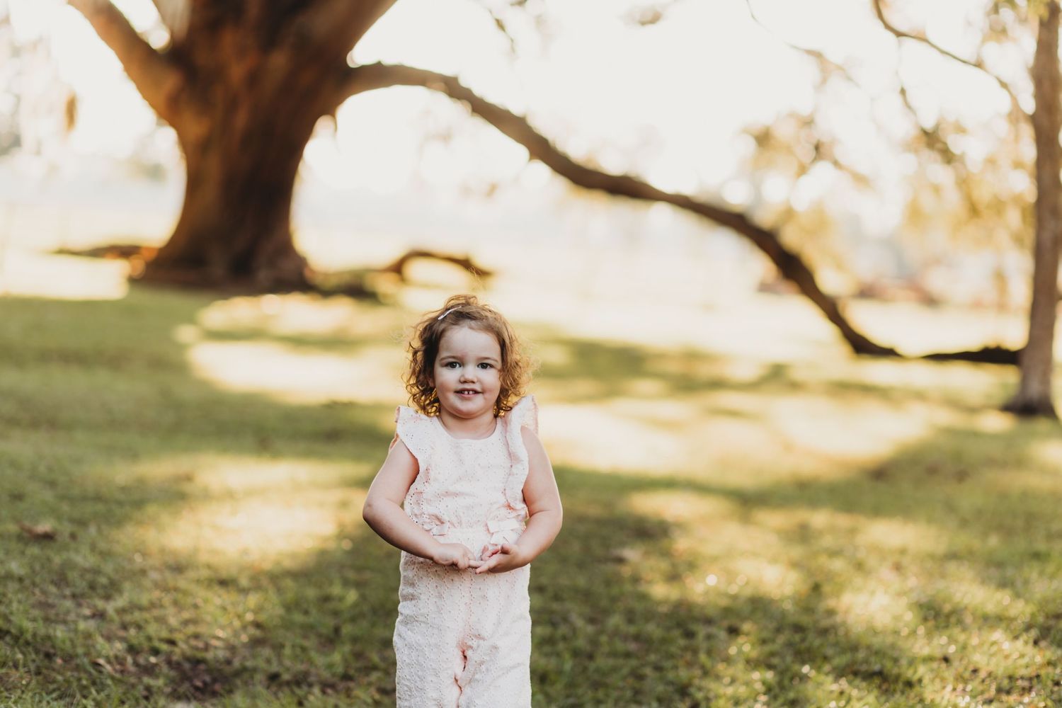 Little girl in pink dress twirls and plays during sunset outdoor photo session.