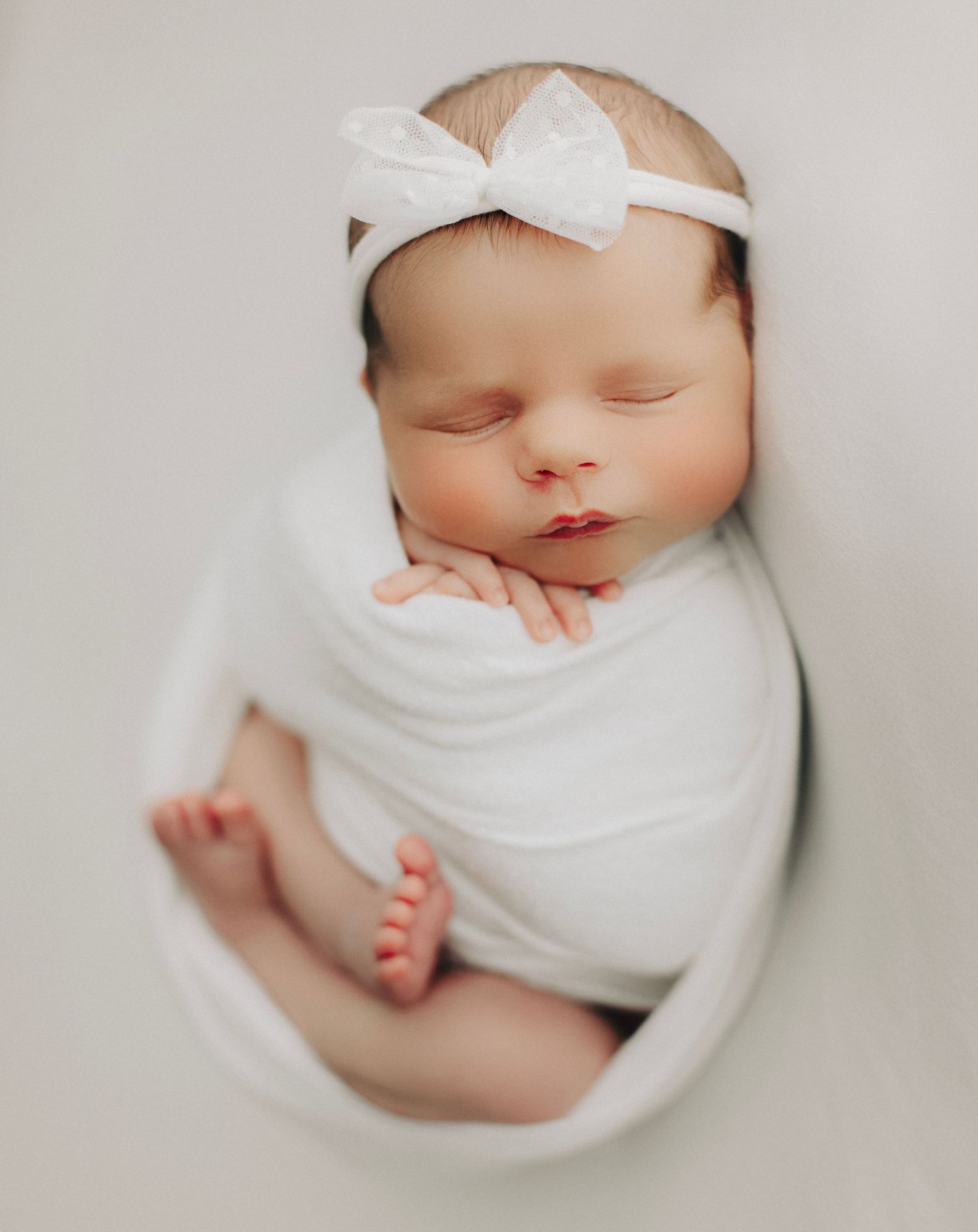 Sleeping baby wrapped in white swaddle with bow headband.