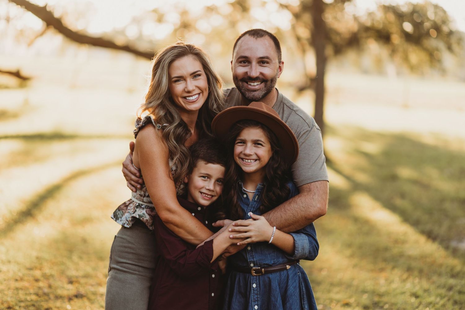 Family of four embracing and smiling during golden hour outdoor photoshoot.