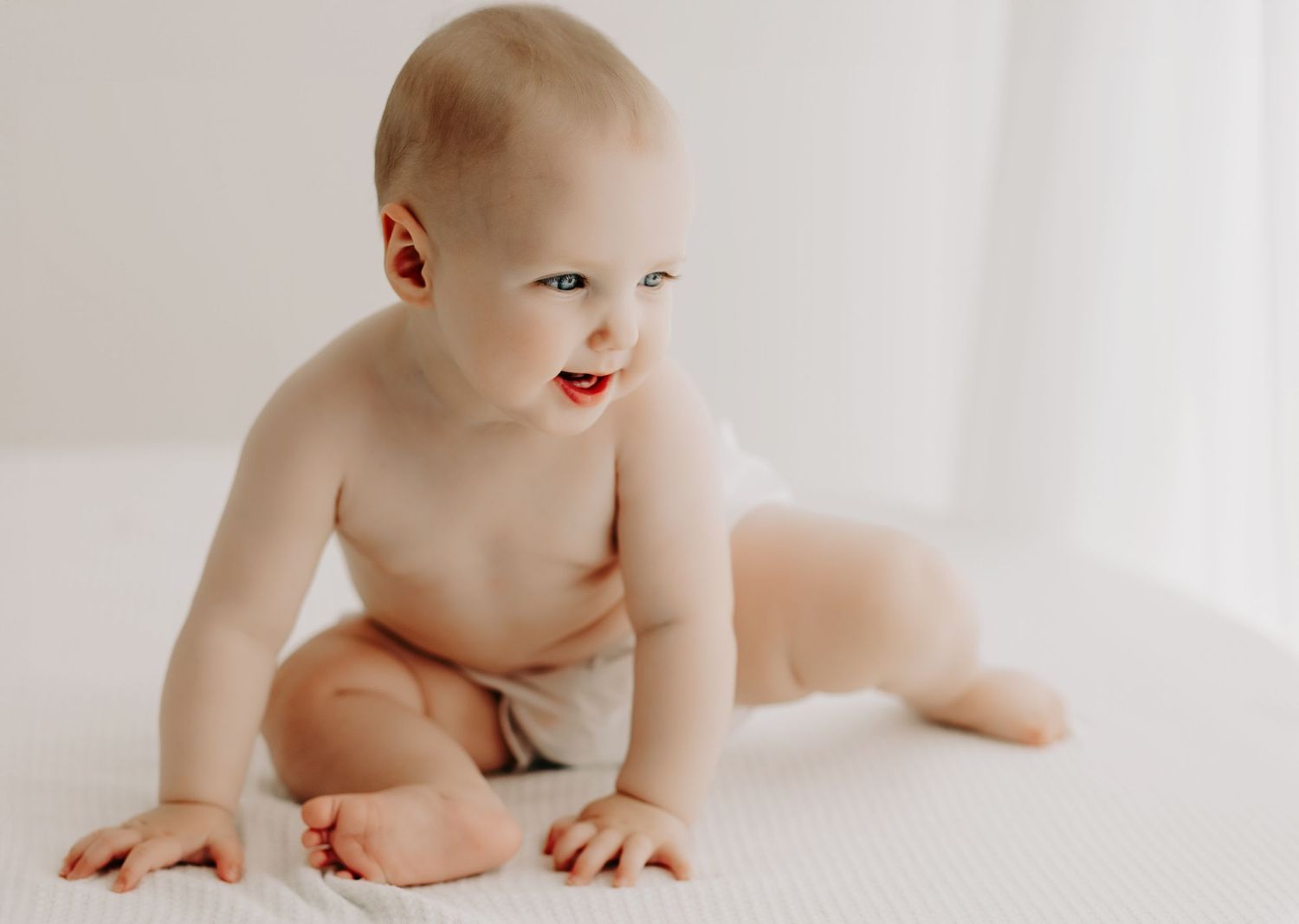 Happy baby in diaper crawling on white surface.