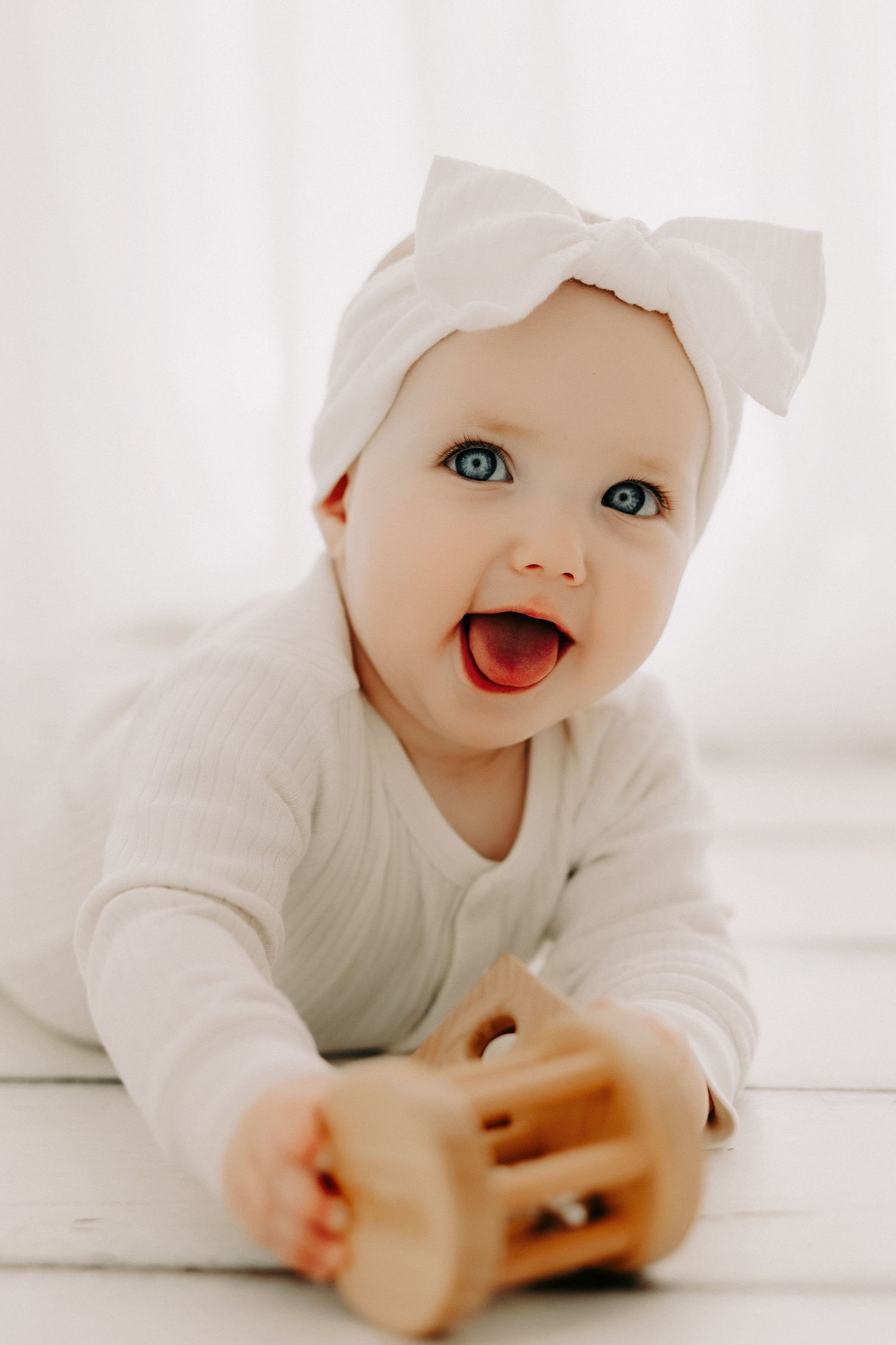 Happy baby in white clothing playing on floor with bright eyes and cheerful expression.