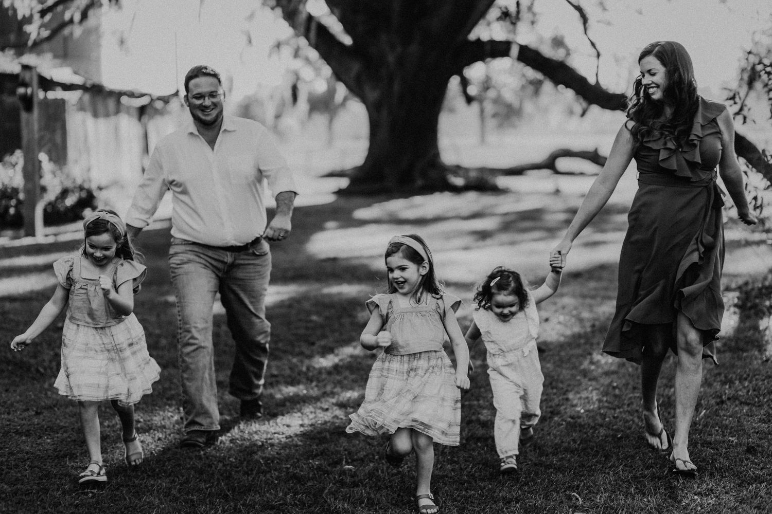 Black and white photo of children running and playing on grass during family photoshoot.