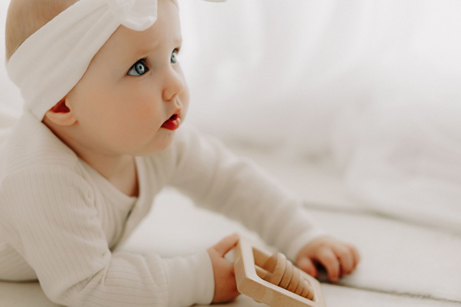 Baby dressed in all white crawls and explores wooden toys on floor.