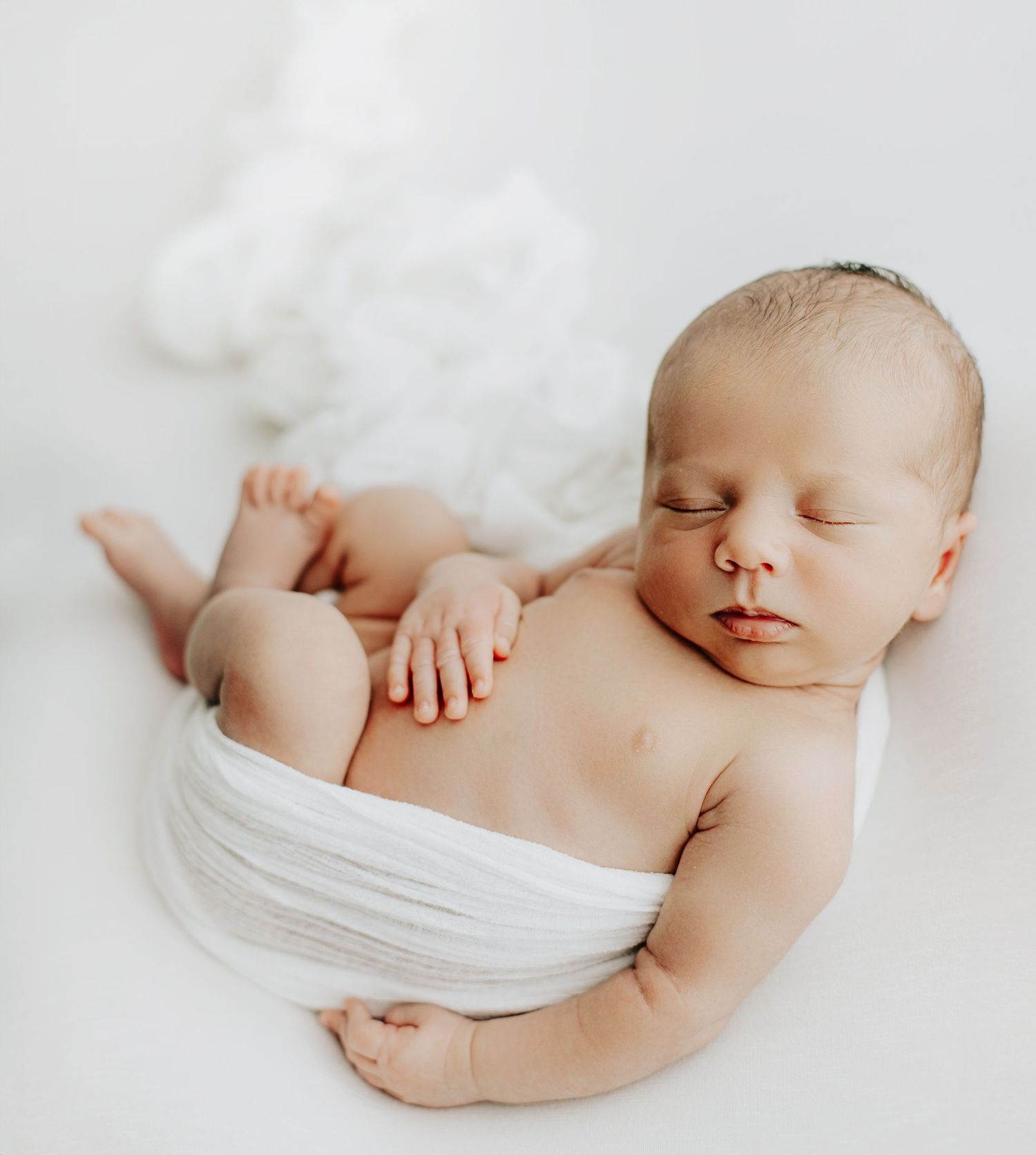 Sleeping newborn baby wrapped in white fabric on light background.