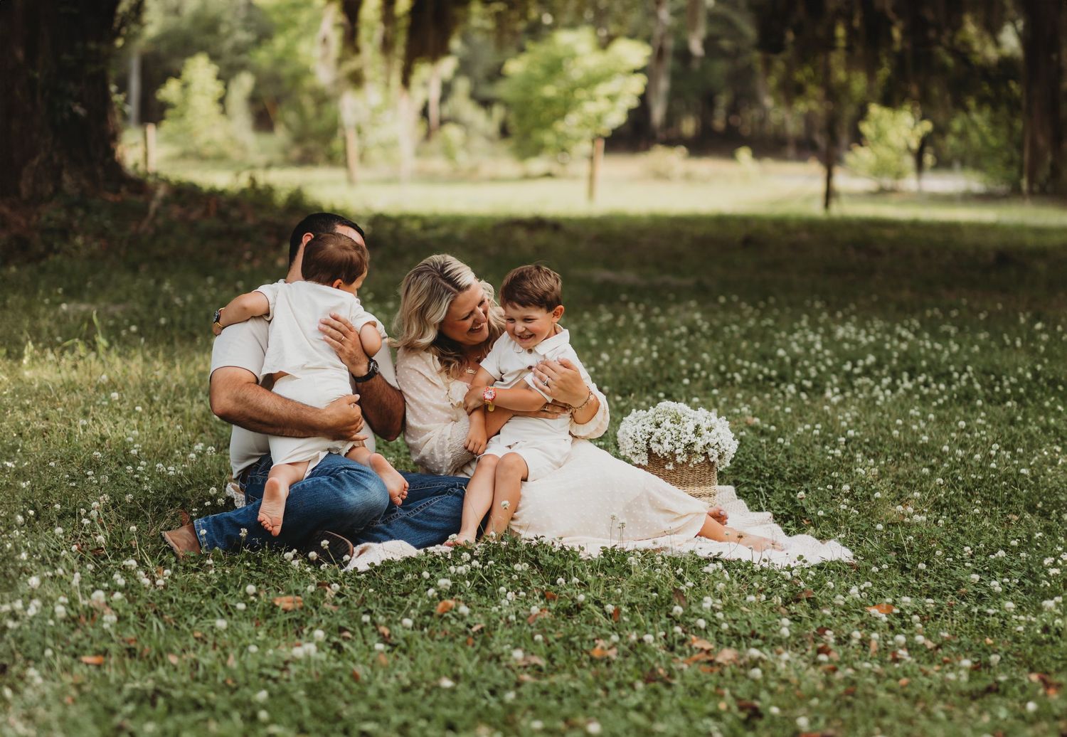 Family cuddles together on a blanket in a scenic park setting with wildflowers.