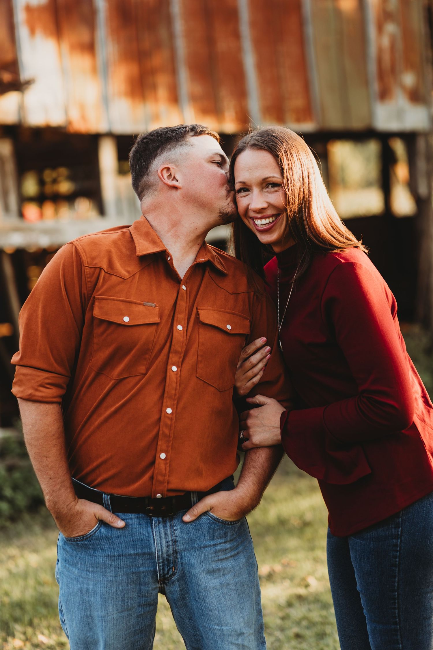 Couple wearing burgundy and rust colored tops share intimate laughing moment outdoors.