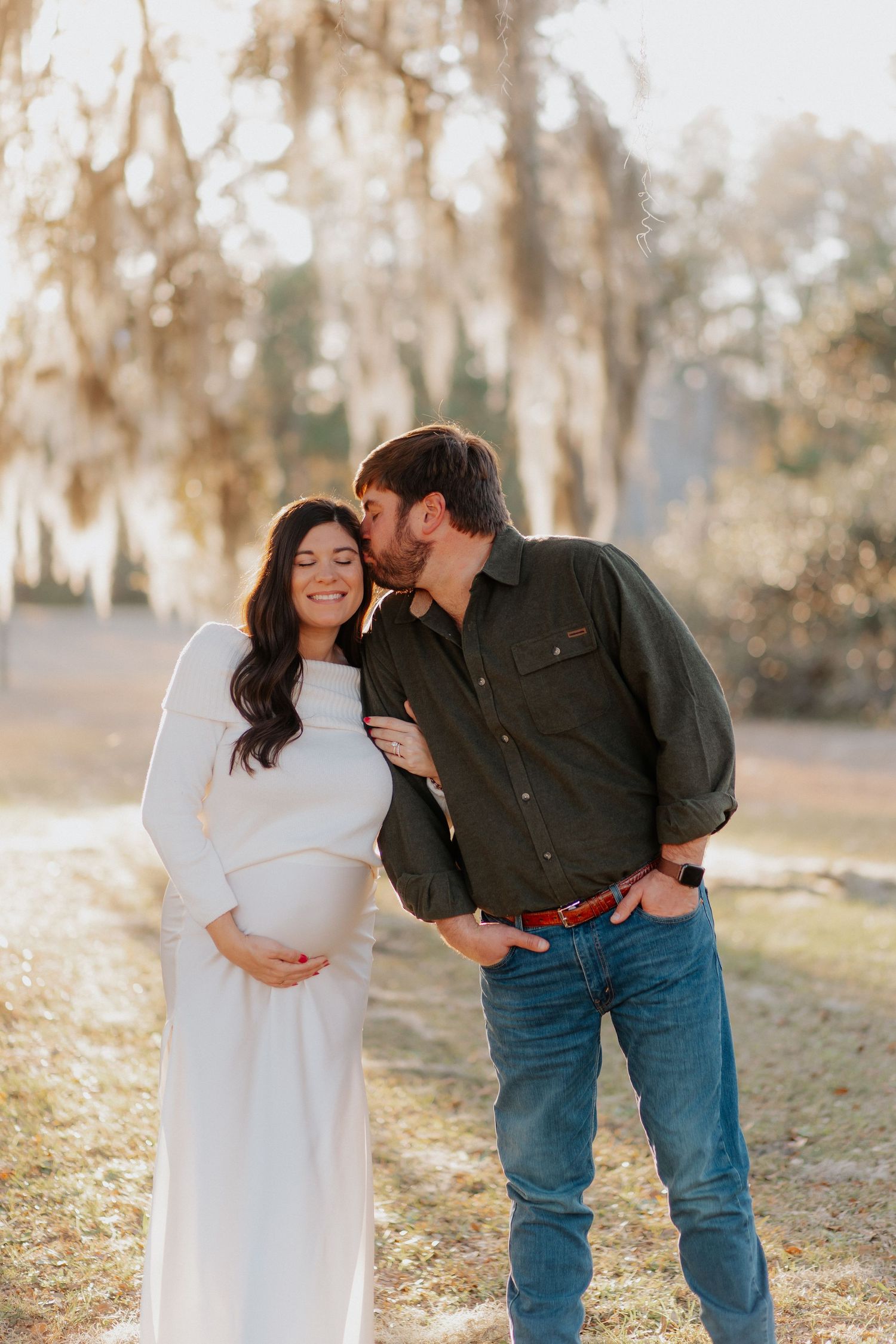 Sweet couple shares intimate moments under moss-laden trees during a sunset photoshoot.