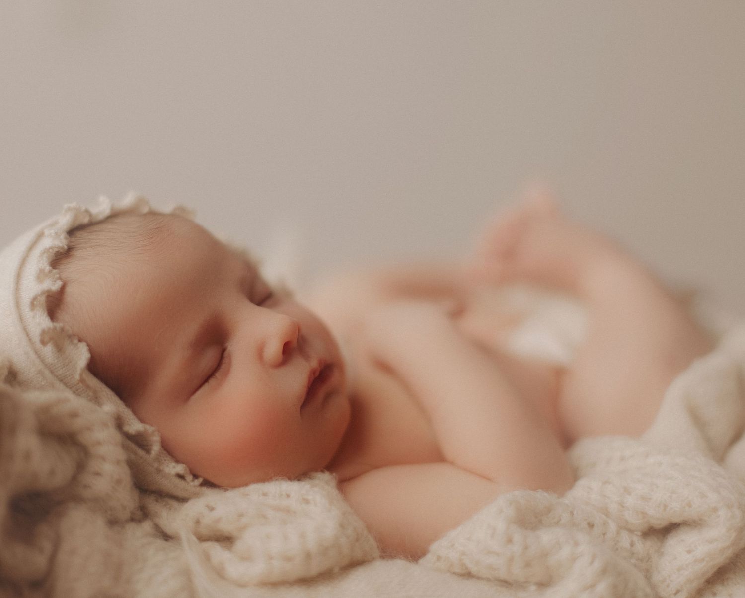 Sleeping newborn baby wrapped in delicate lace on soft taupe background.