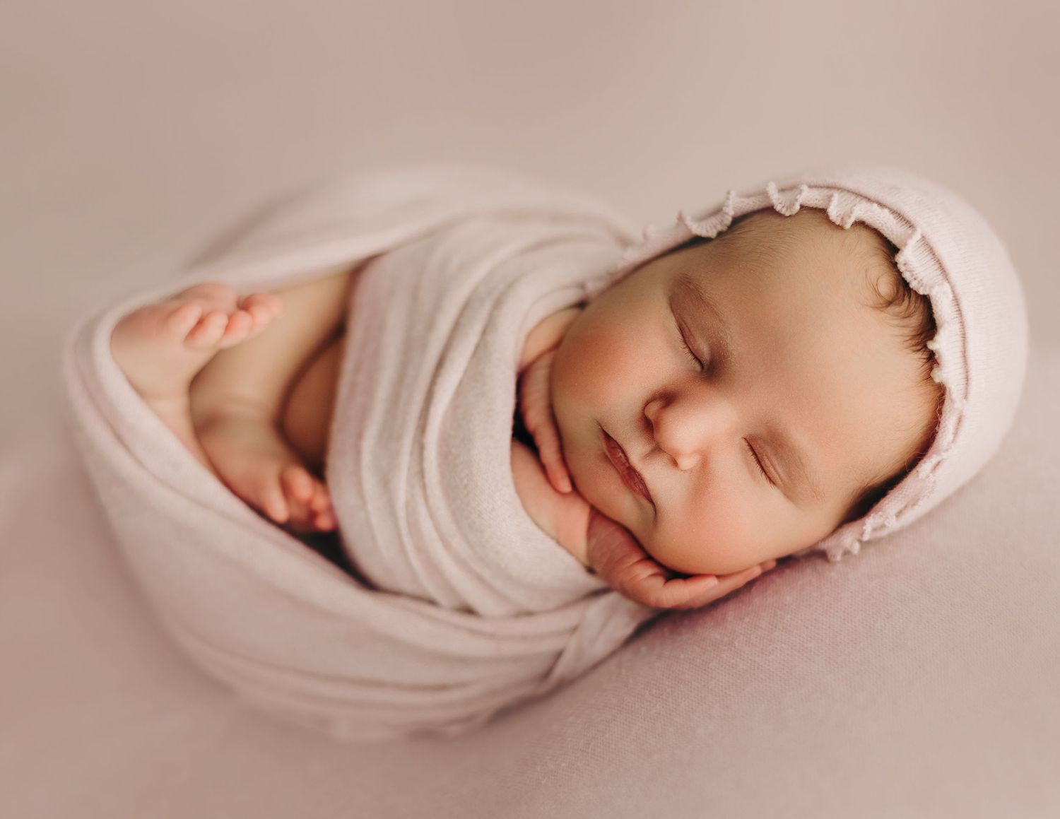 Sleeping infant wrapped in white swaddle blanket rests peacefully in studio light during newborn photography session.