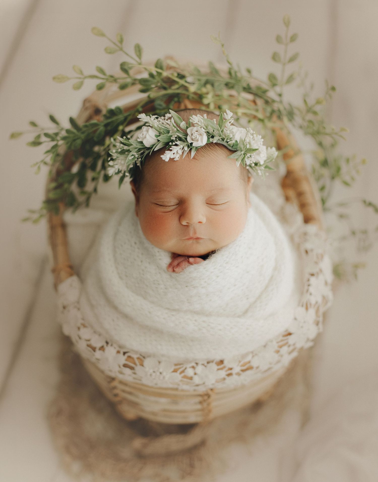 Sleeping newborn with leafy crown wrapped in white in rustic basket.