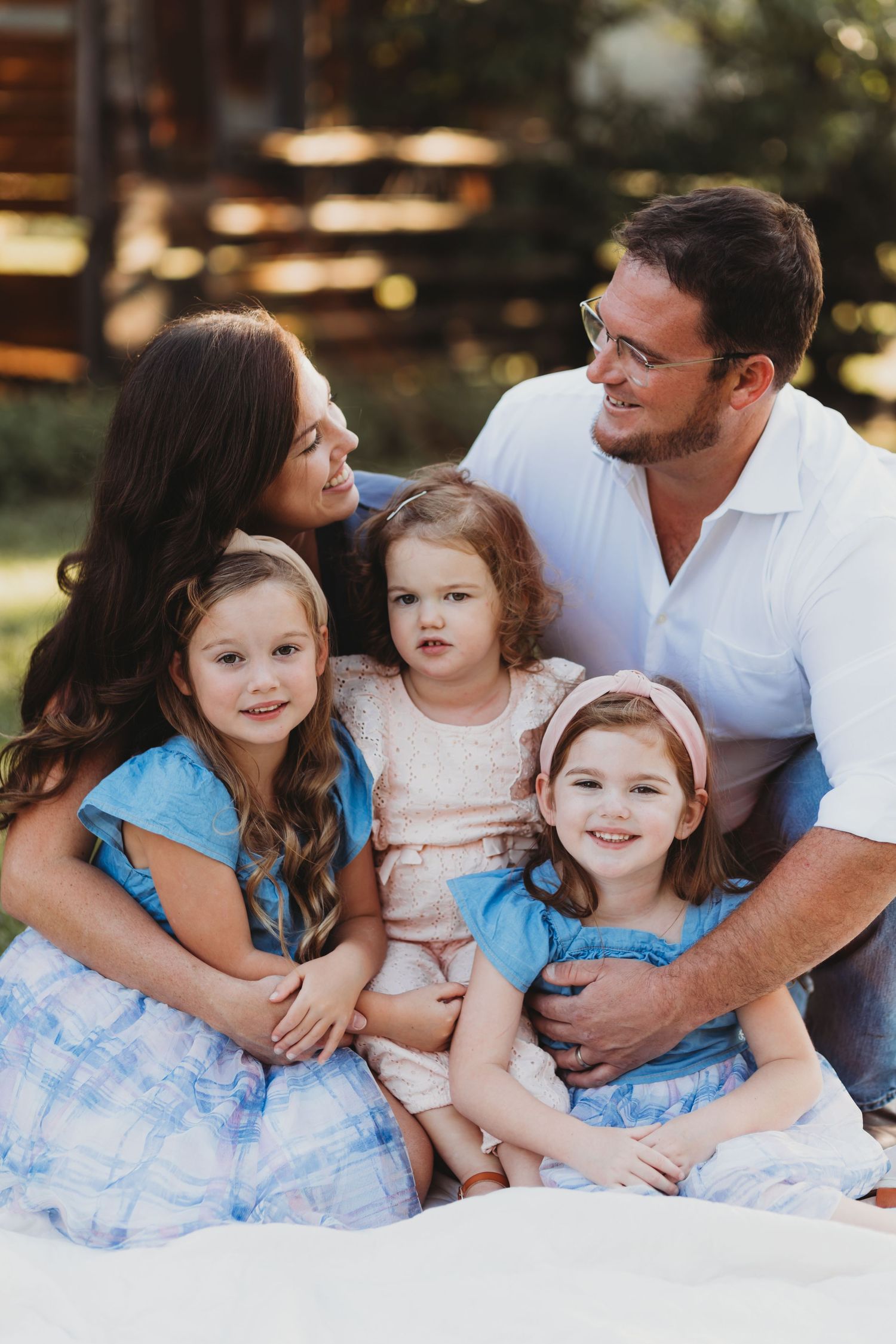 Family lounging together on white blanket during outdoor photo session in casual attire.