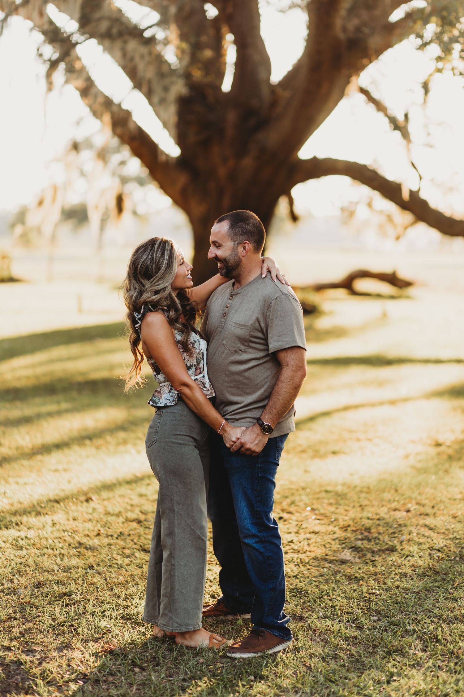 Couple sharing intimate moment under large tree during sunset photoshoot.