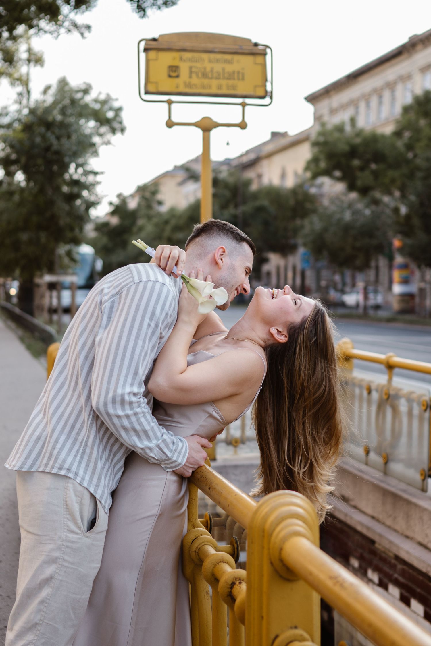 Romantic couple poses on a yellow railing in an urban setting during a photoshoot.