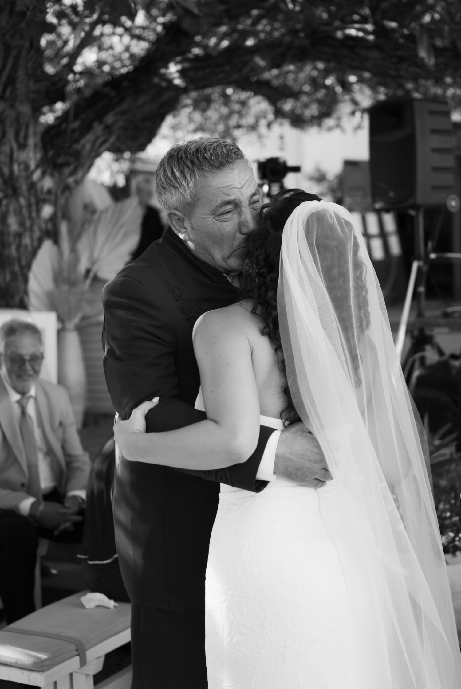 Father of the bride shares tender embrace with daughter in wedding gown at outdoor ceremony.