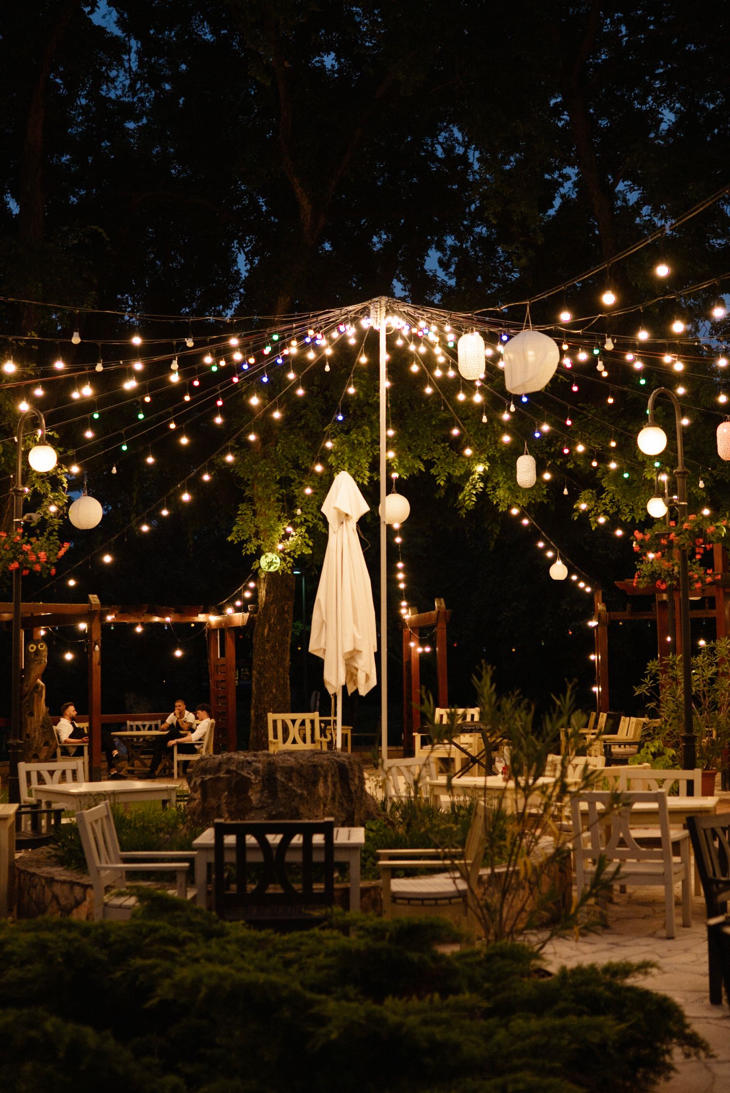 Enchanting outdoor wedding reception at night with string lights and paper lanterns illuminating garden seating area.