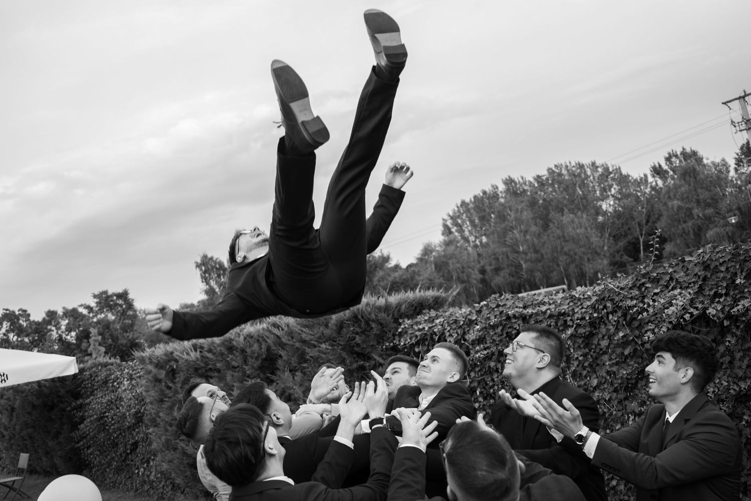 Wedding guests perform acrobatic jumps and flips outdoors.
