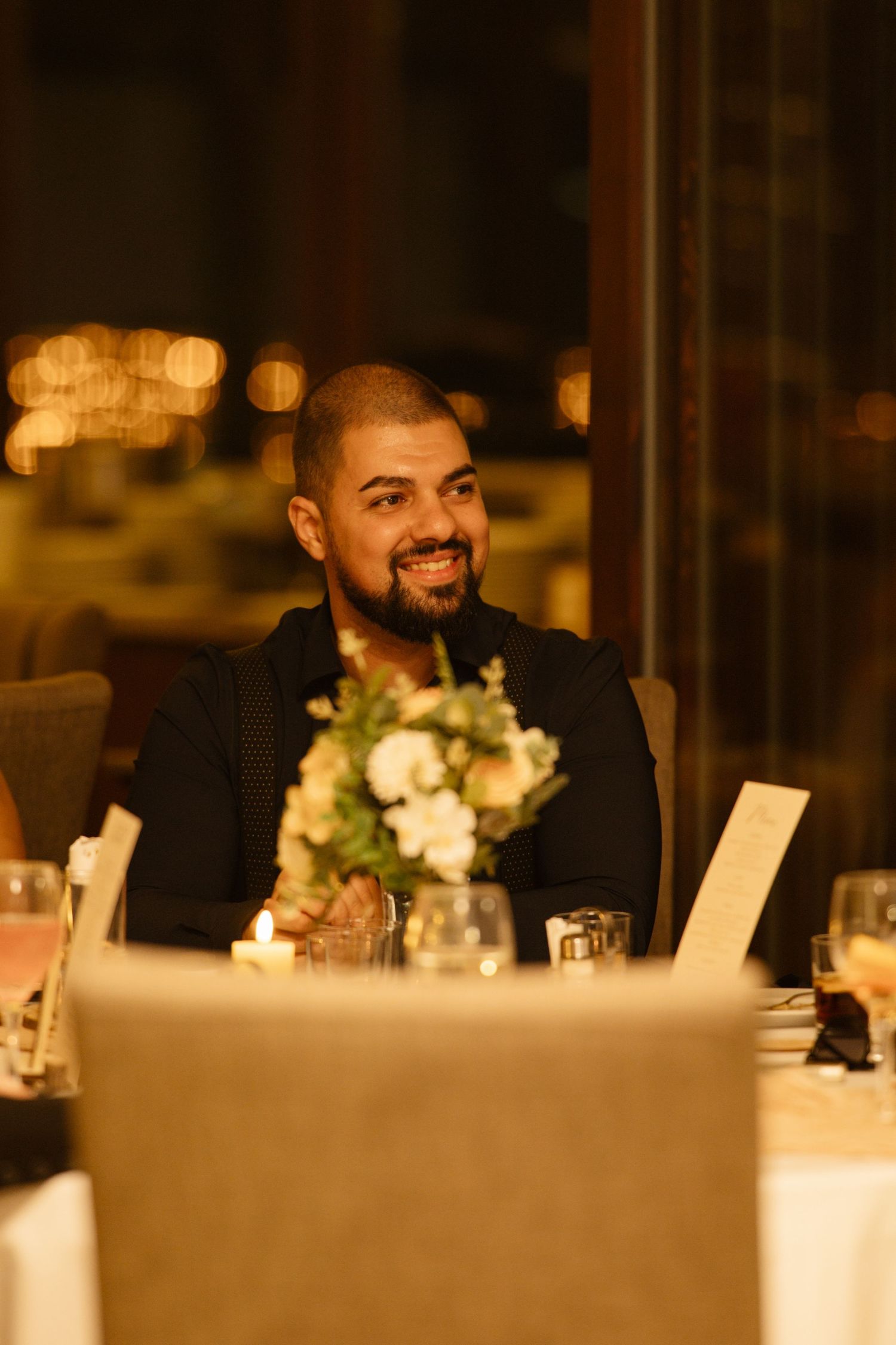 Wedding reception guests seated at tables with warm lighting and floral centerpieces.