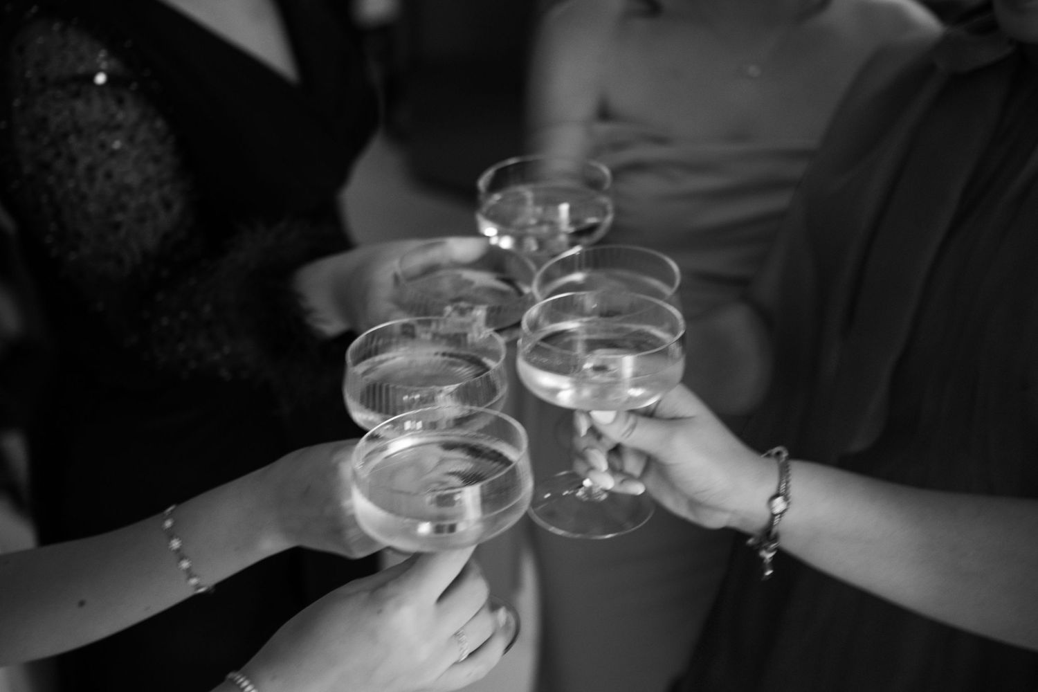 Hands holding wine glasses together in a celebratory toast against dark background.