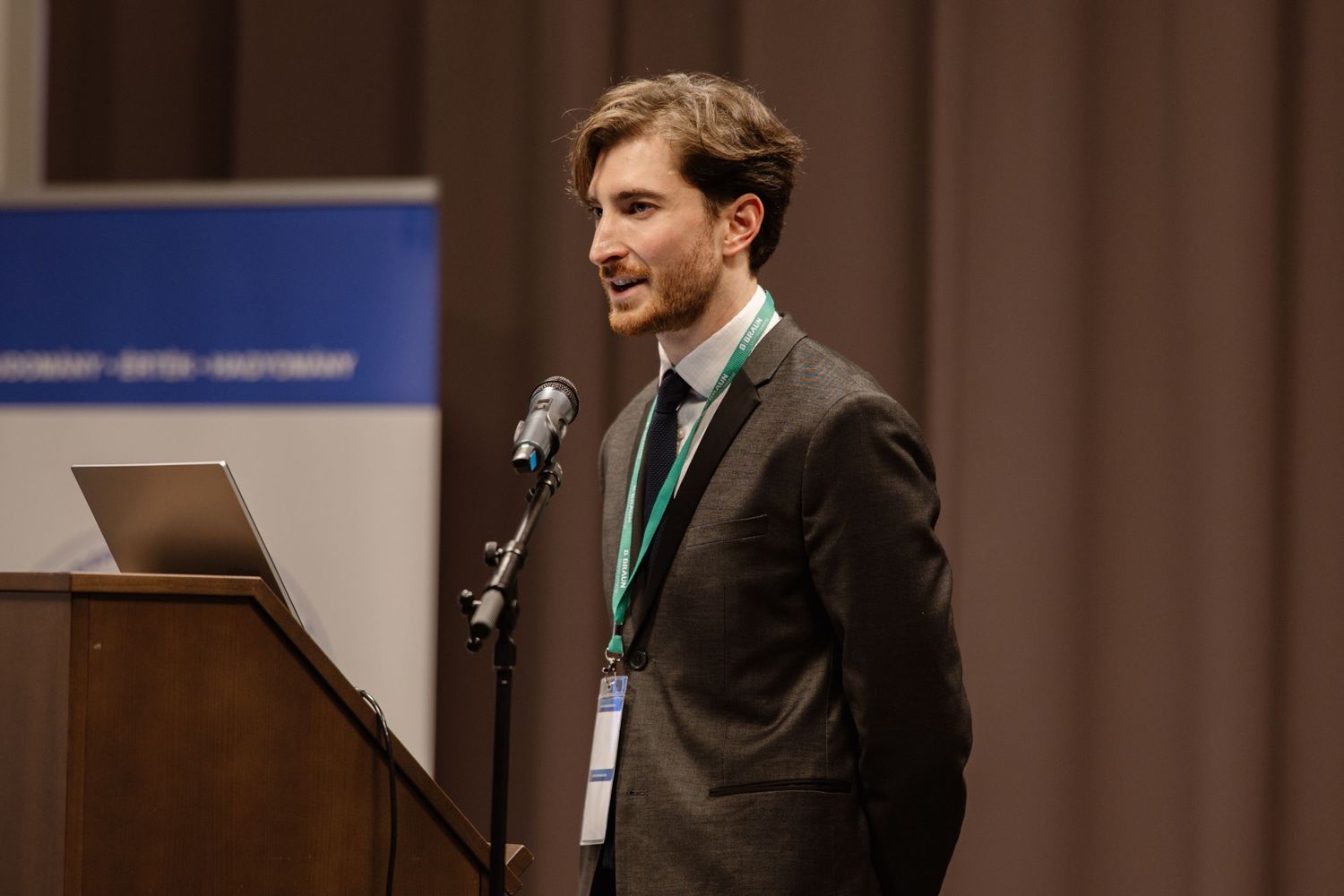 Presenter speaking at podium with laptop during conference presentation.