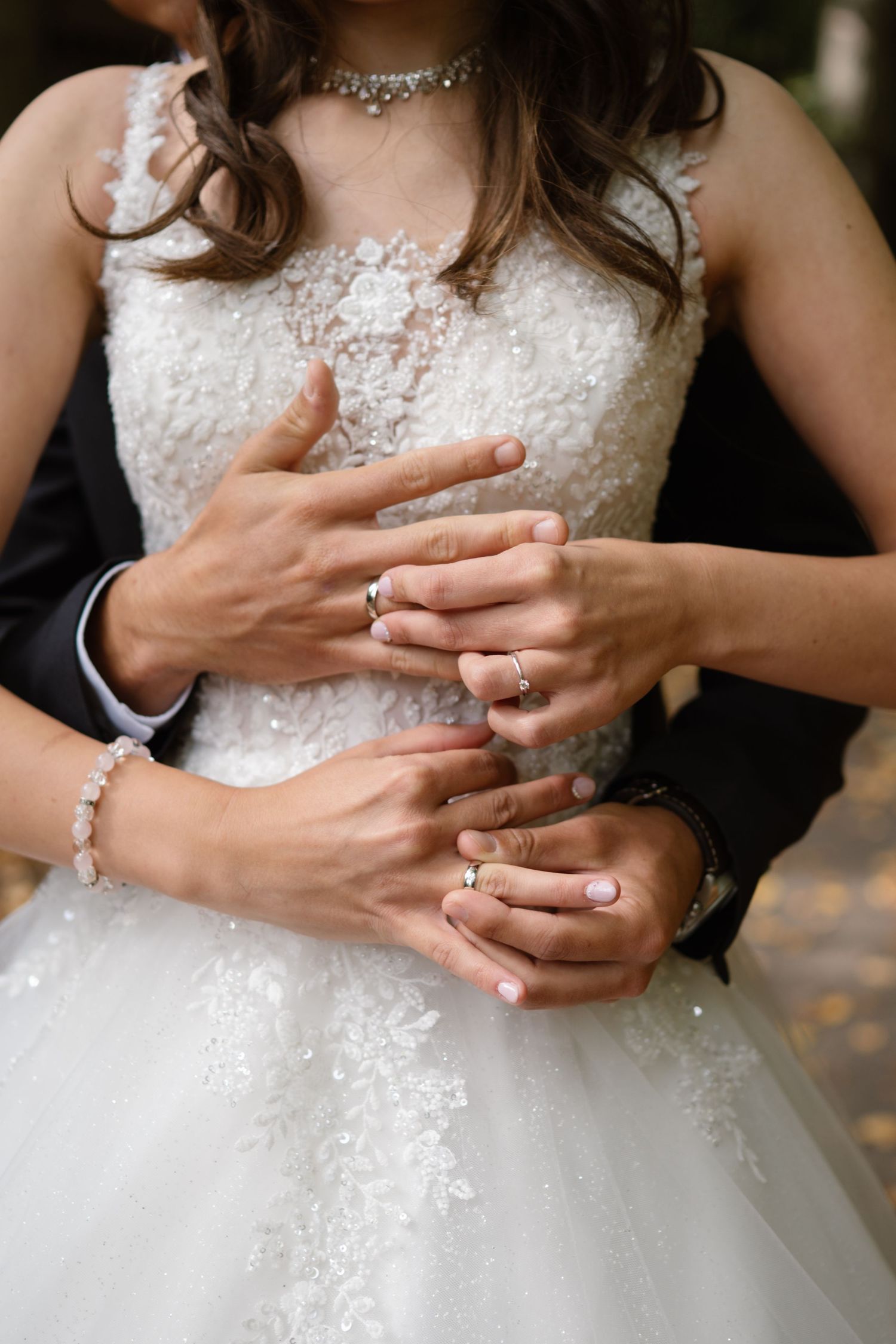 Close-up of hands with wedding rings resting on a white lace wedding dress.