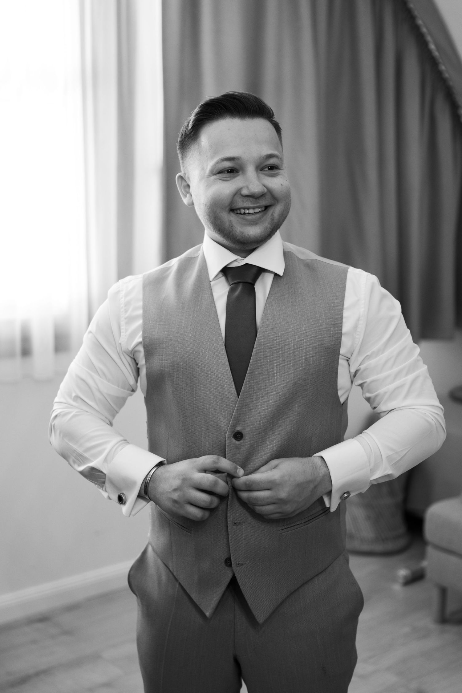 Person adjusting grey vest while getting dressed for formal occasion.