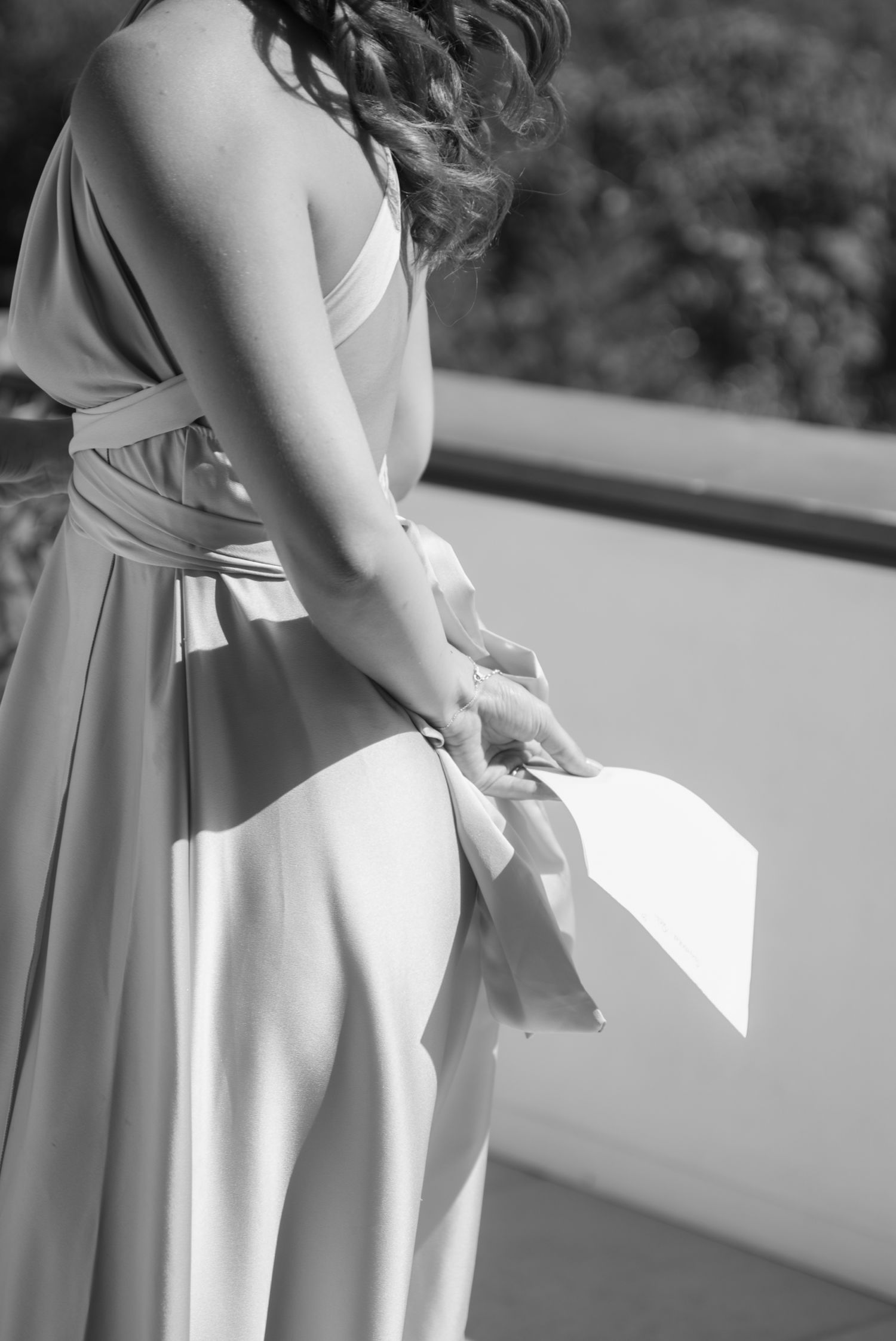 Black and white photo of a woman in an elegant halter gown with flowing ribbons, standing on a balcony.