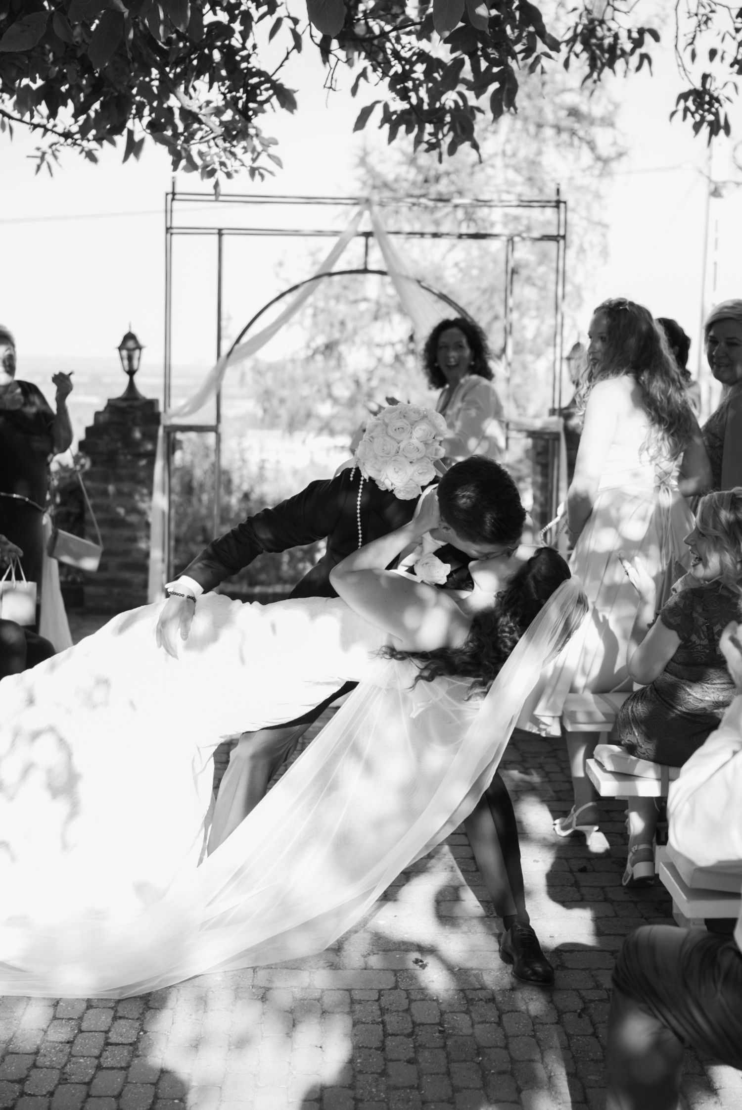 Black and white photo of a groom dipping his bride for a kiss at an outdoor wedding ceremony.