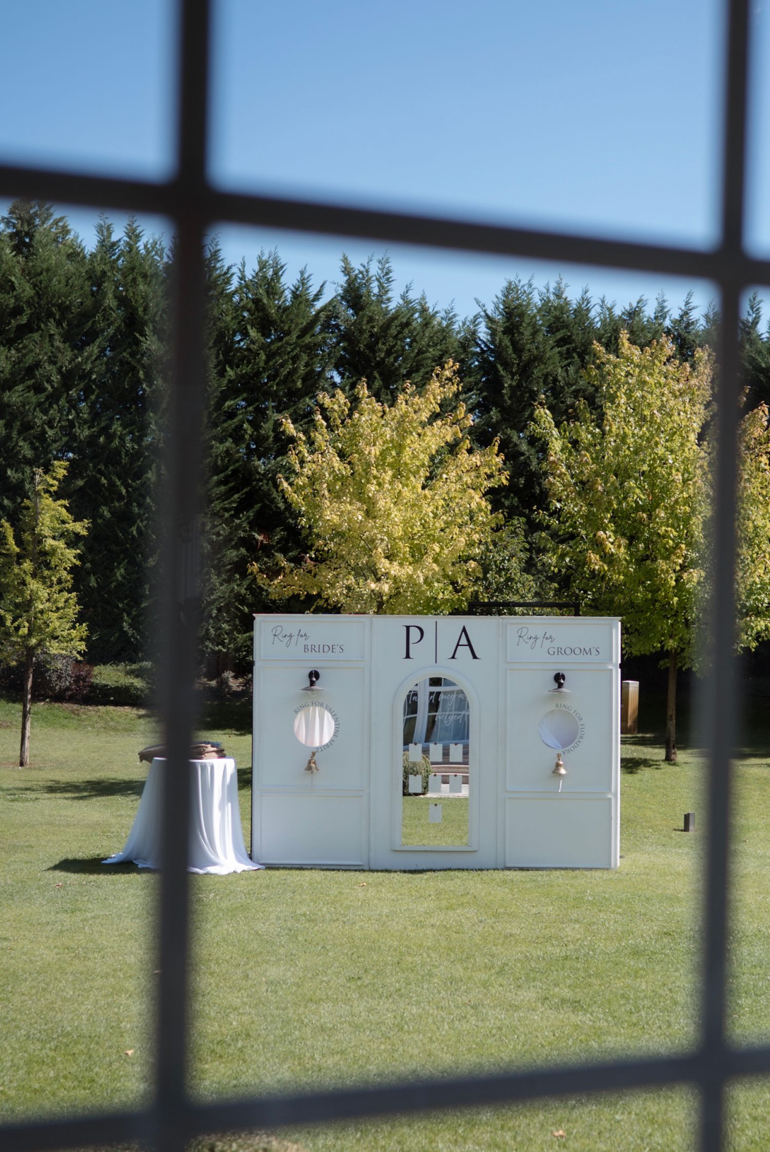 Elegant outdoor wedding sign with monogram P|A on white display stand, surrounded by lush green trees on a sunny day.