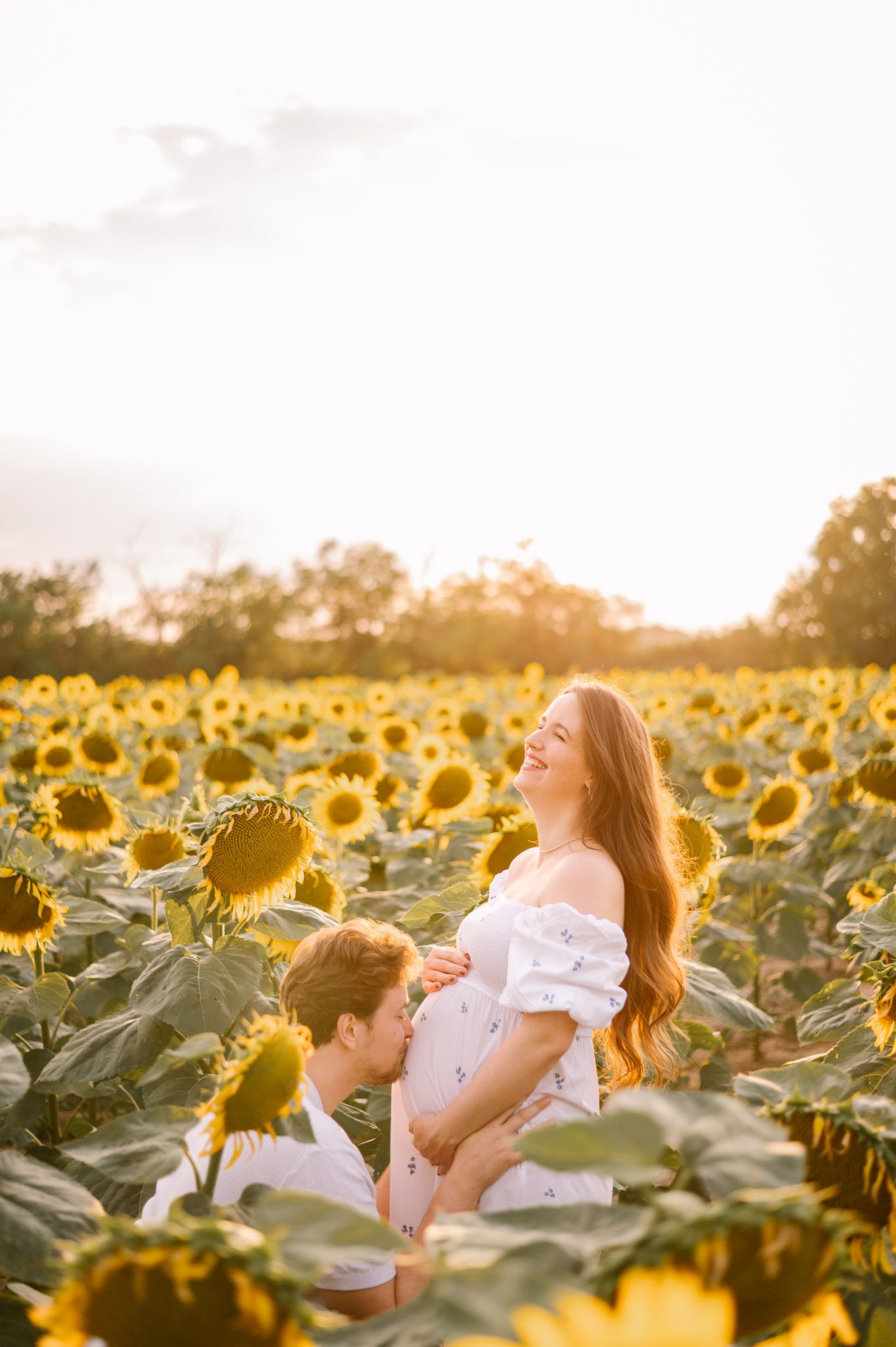 Romantic maternity photo in a sunflower field at golden hour.
