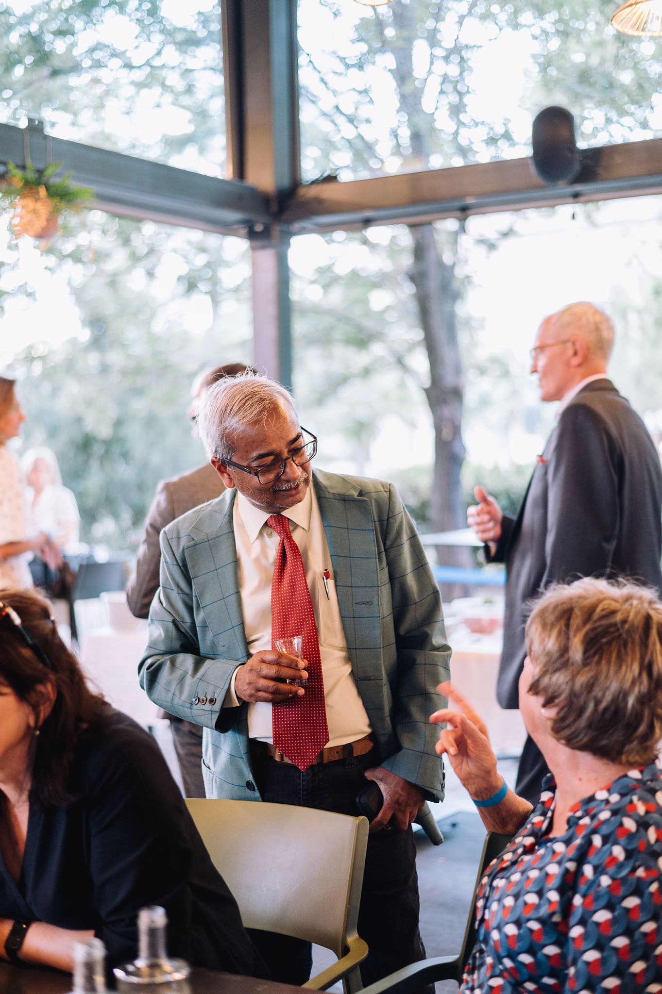 Professional networking event with attendees conversing in a venue with large windows.