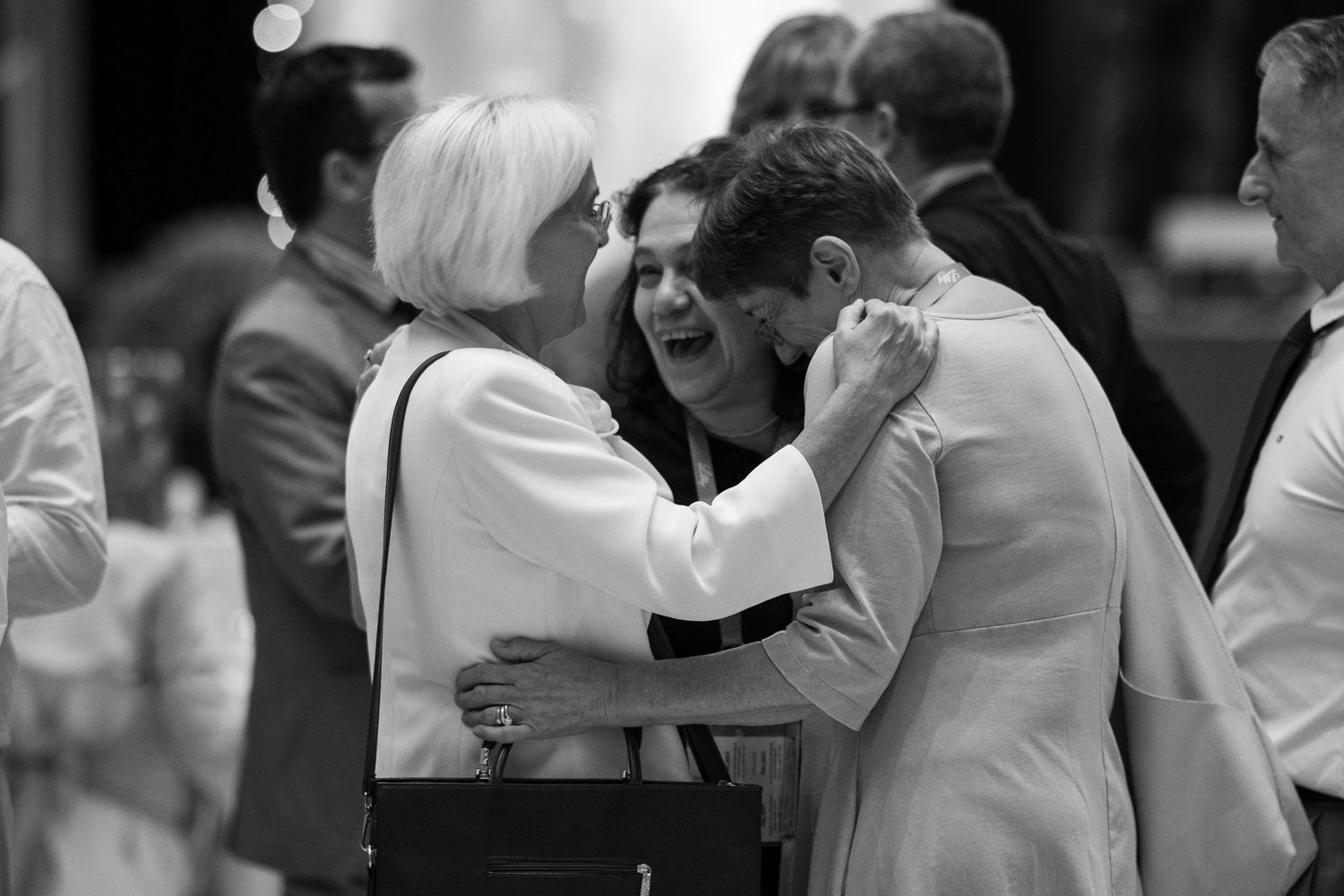 Black and white photo of attendees embracing at formal gathering.