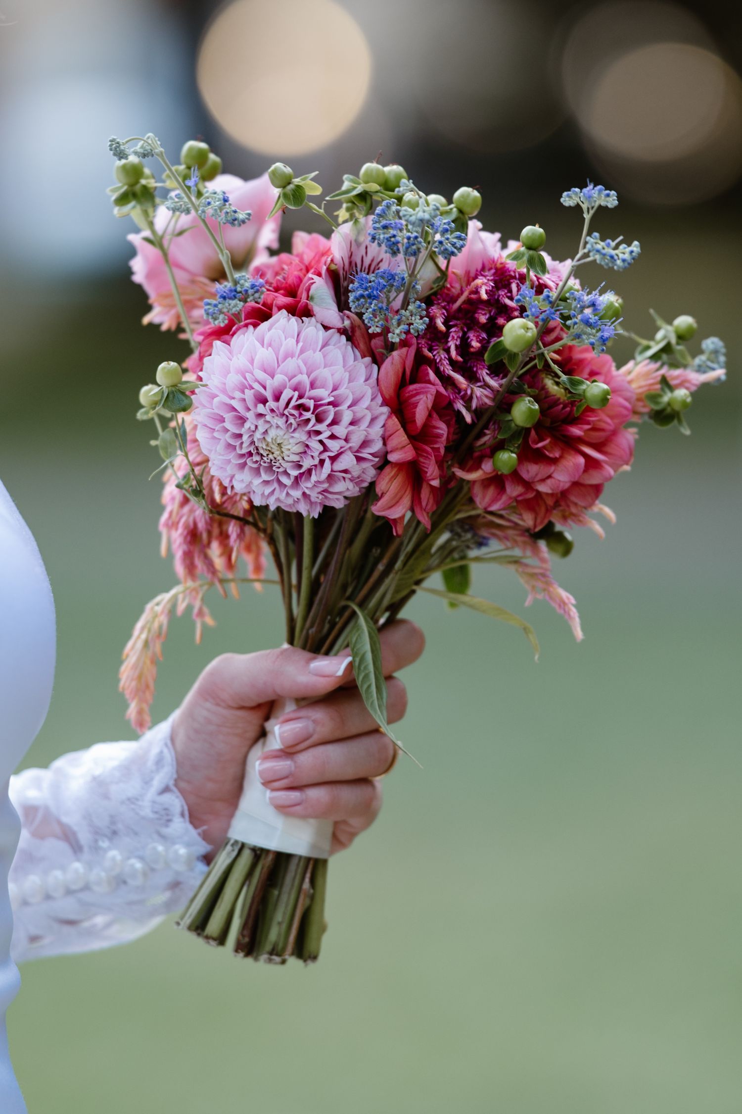 Pink and purple wedding bouquets with dahlias and wildflowers held against a soft bokeh background.