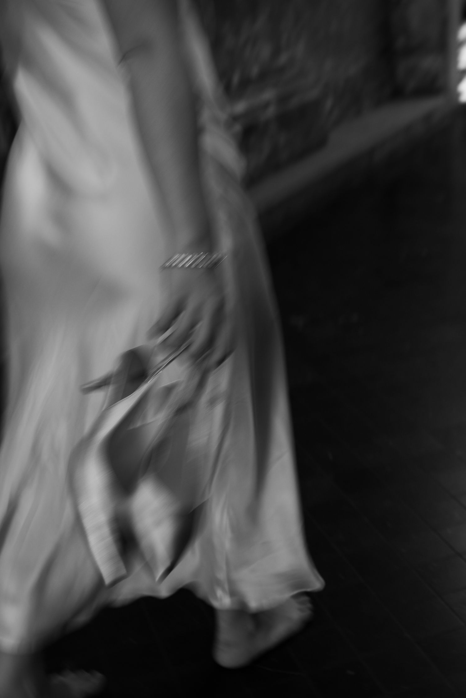 Blurred black and white photo of a woman in a flowing gown, bracelet visible, captured mid-motion.