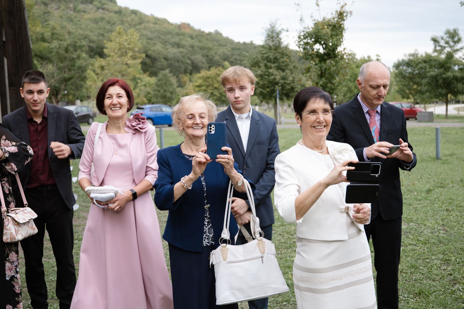Wedding guests in formal attire gather outdoors watching the ceremony.