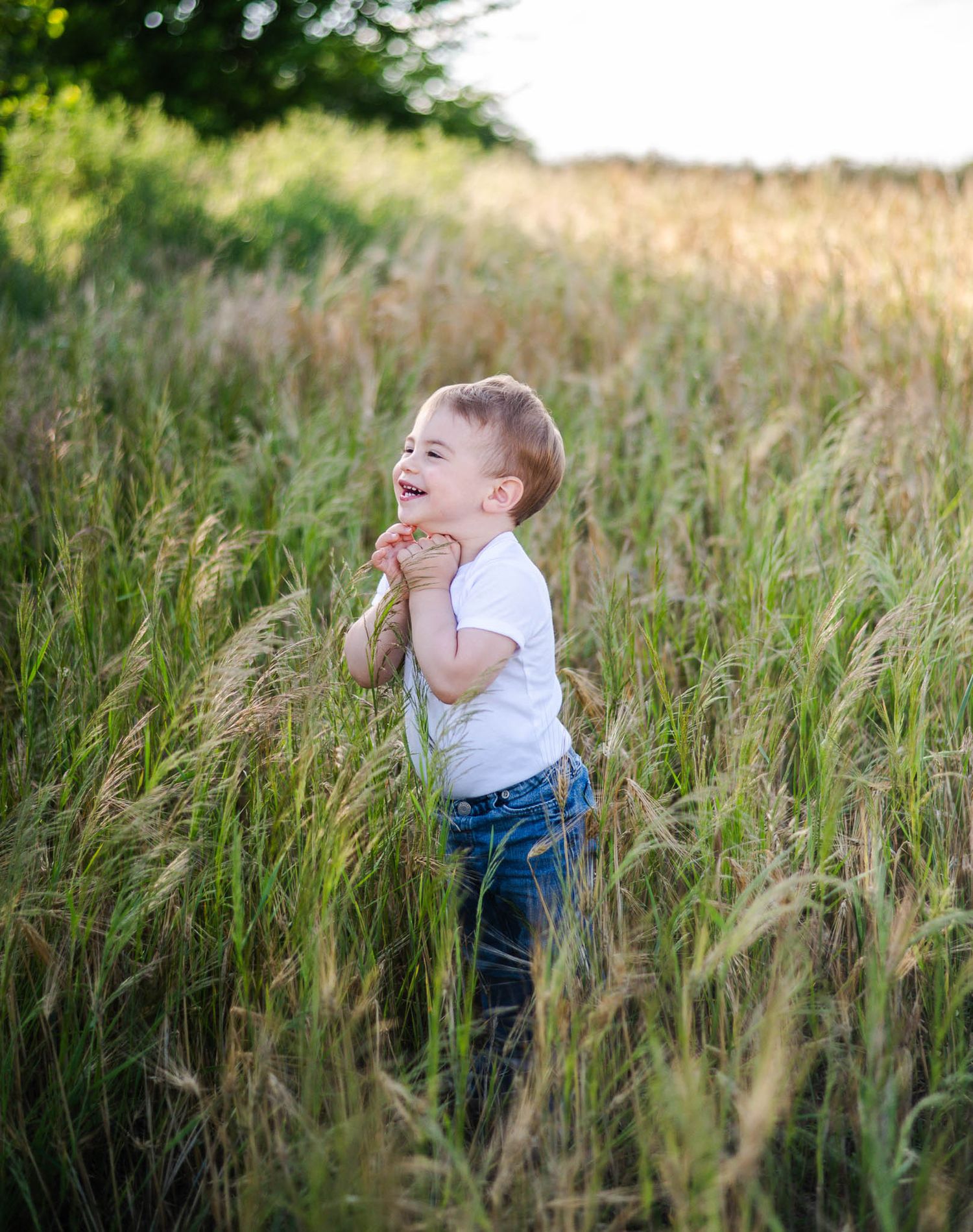 Young child playing and laughing while running through tall grass in a sunny field.