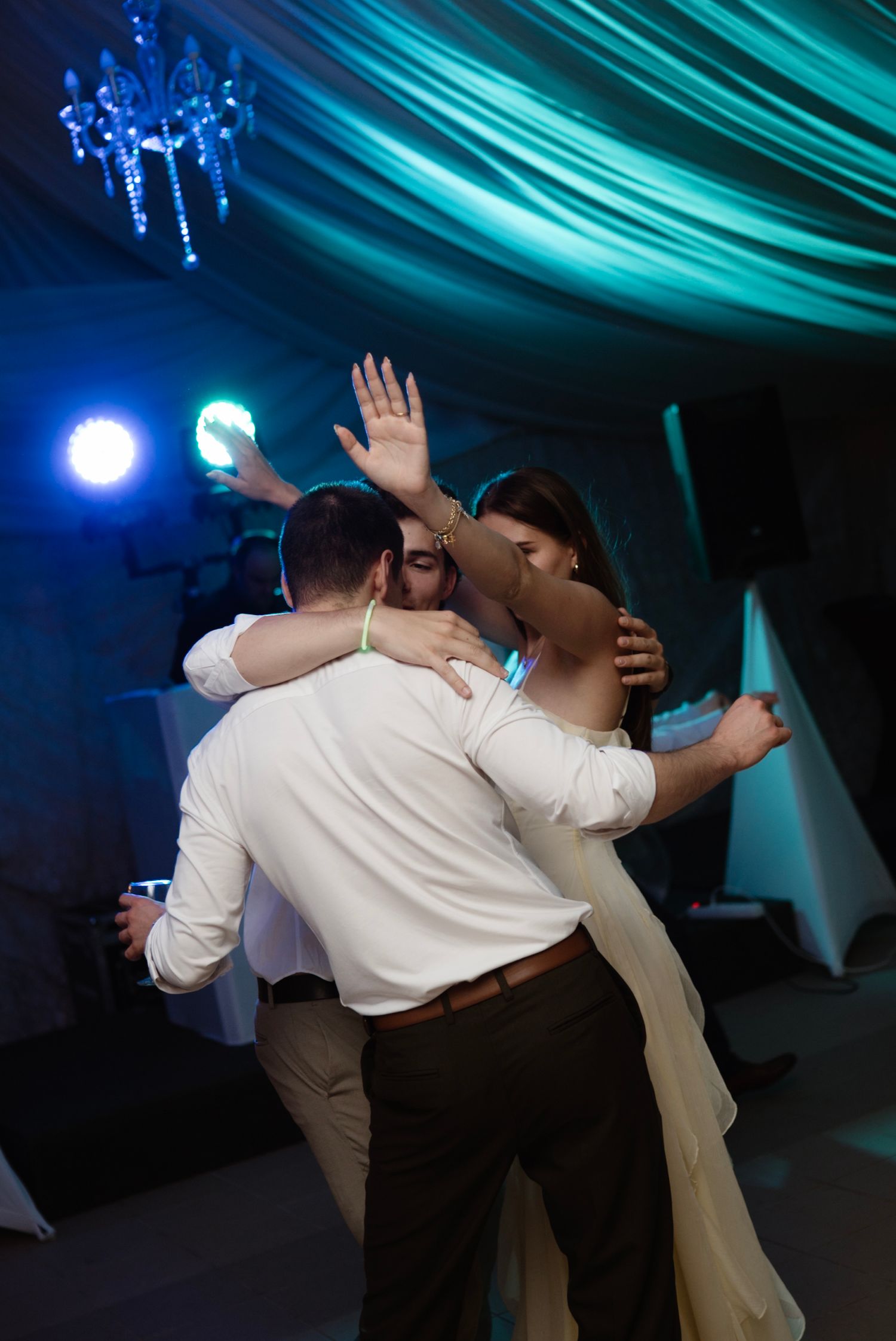 Bride and groom share a romantic embrace on the dance floor under teal lights at their wedding reception.