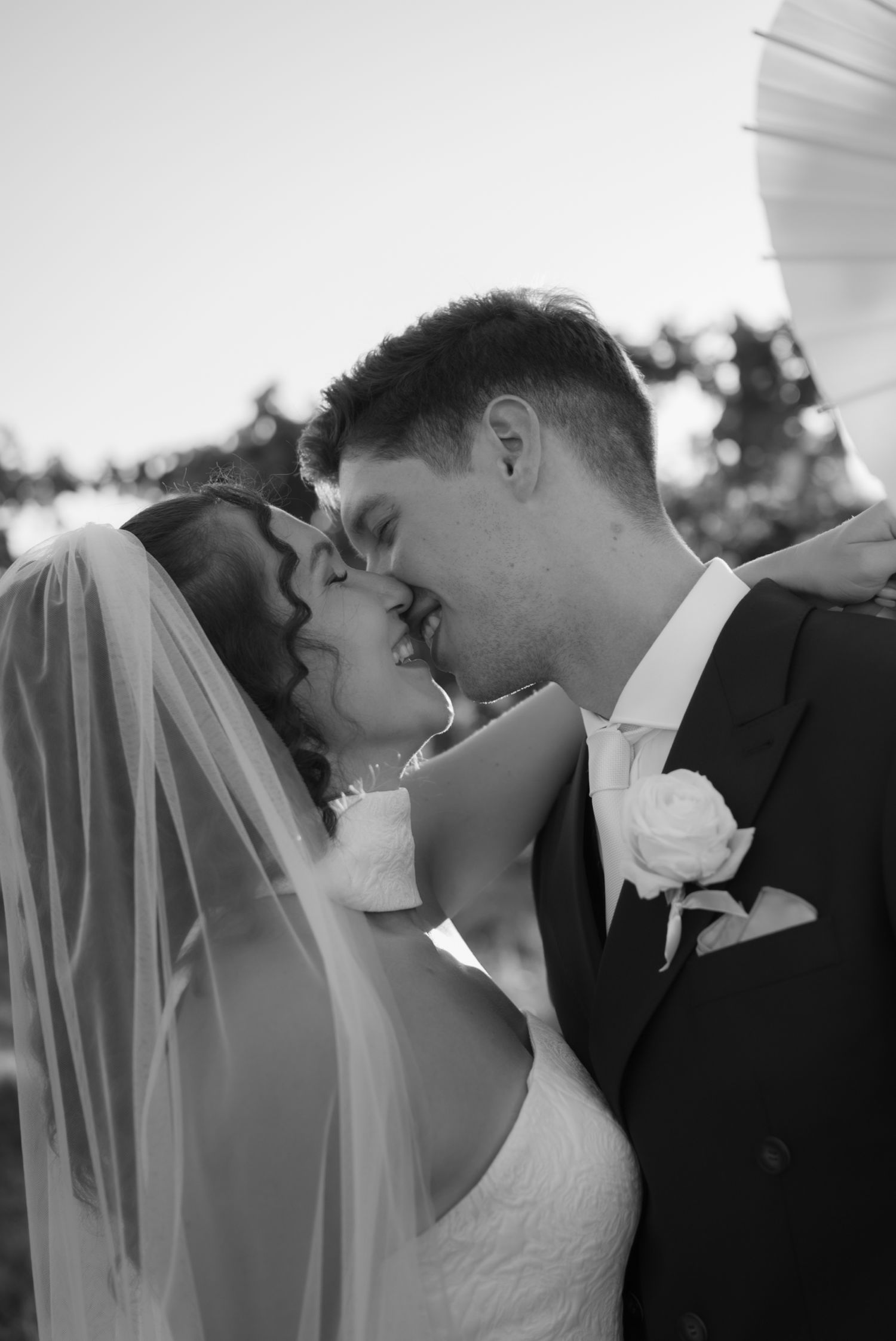 Black and white photo of a bride and groom sharing a romantic kiss at their wedding ceremony.