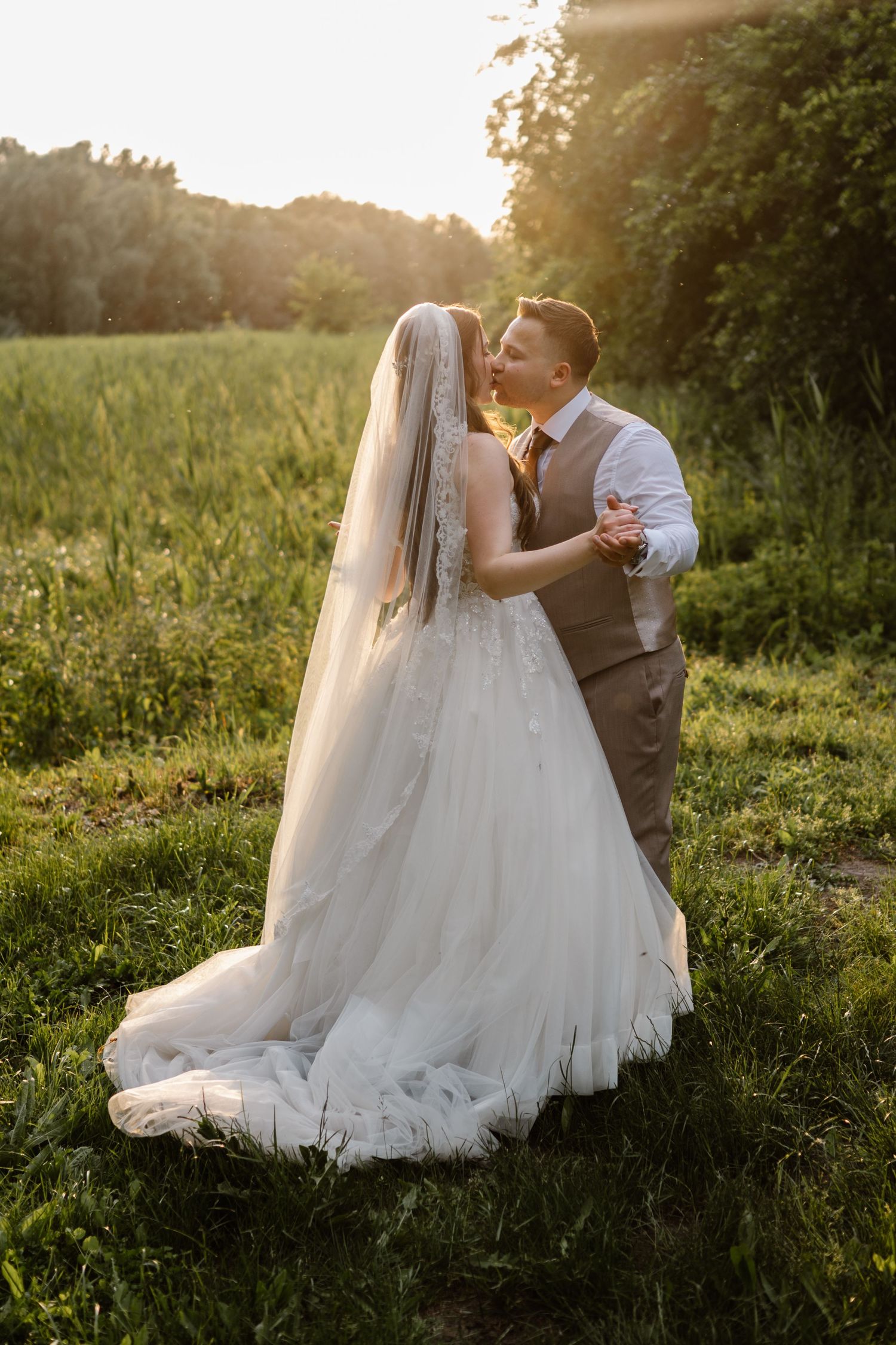Newlyweds sharing a romantic moment in a sunlit field at golden hour.