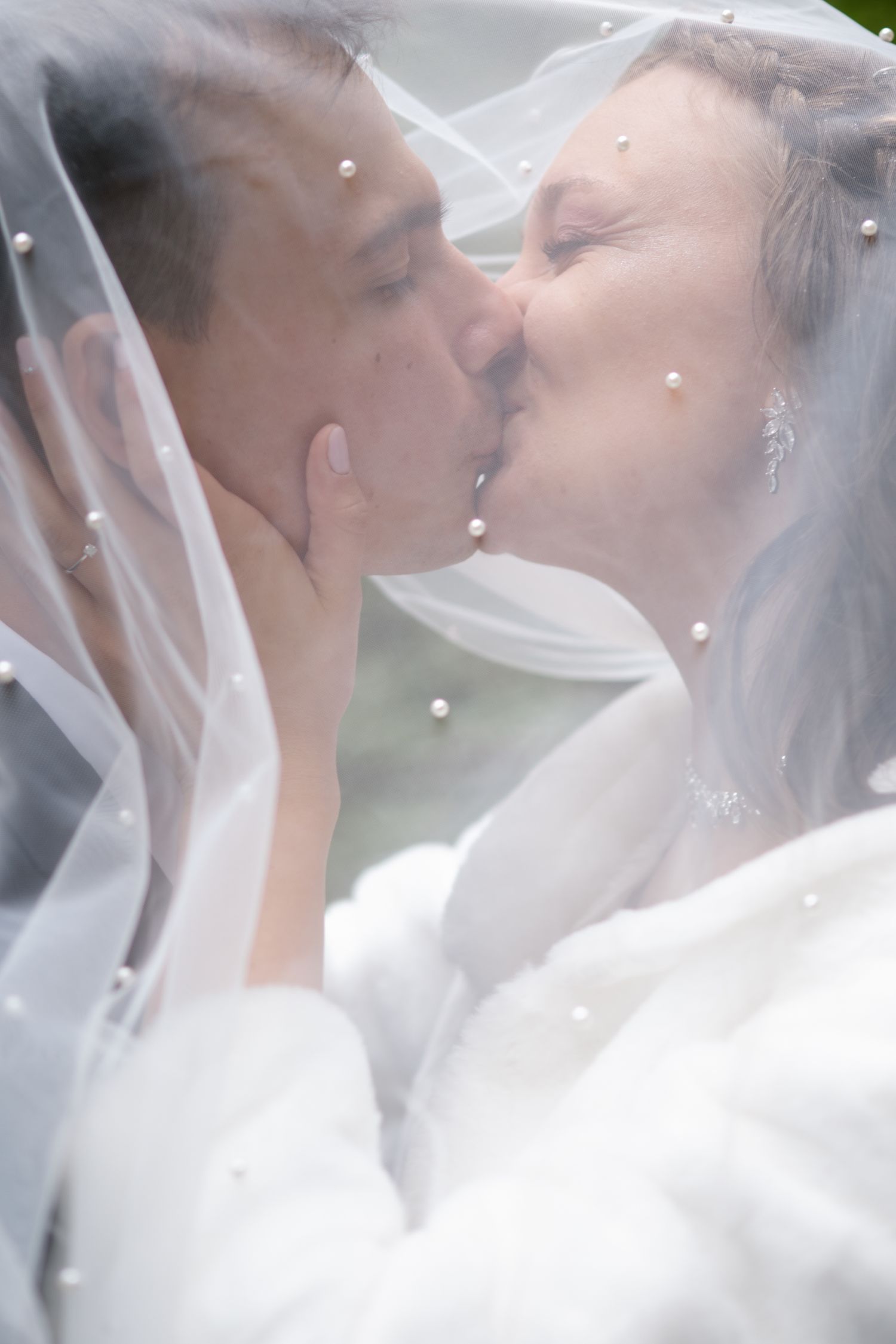 Romantic wedding kiss photos under a delicate white veil with soft lighting.