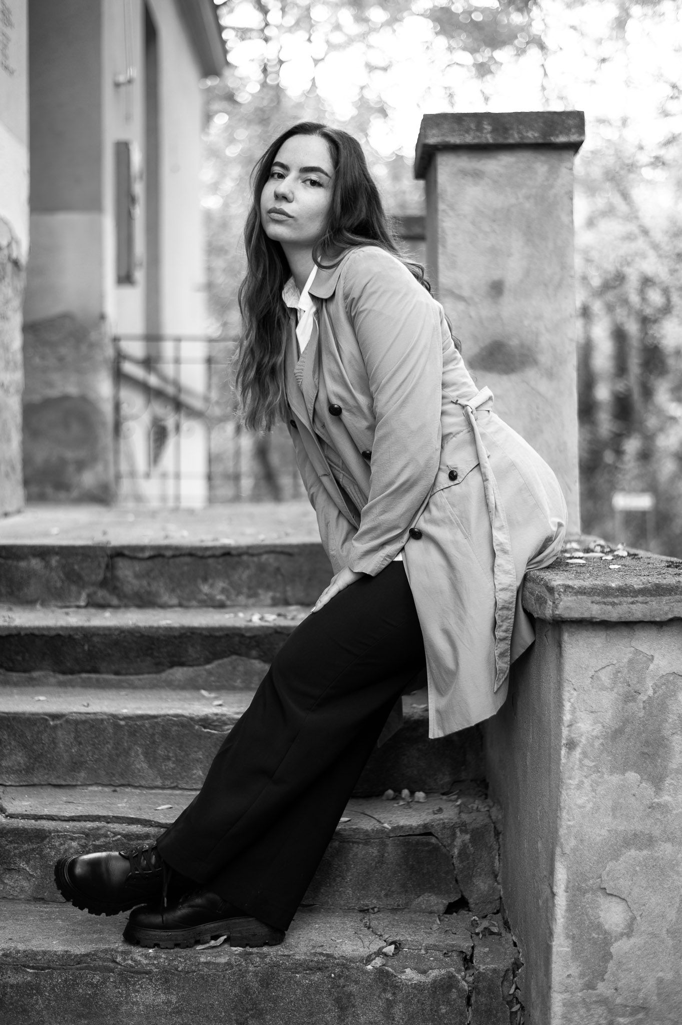 Portrait of woman in trench coat sitting on stone steps in black and white.