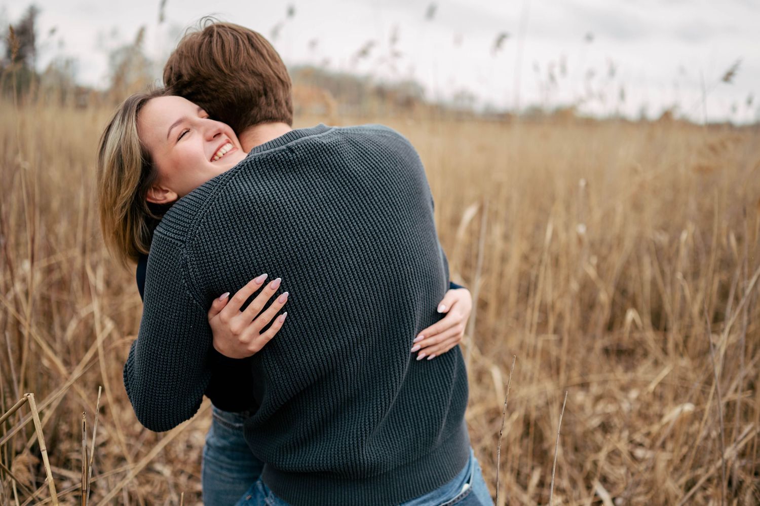 Candid shots of a couple embracing in a rustic field with dried grass in the background.