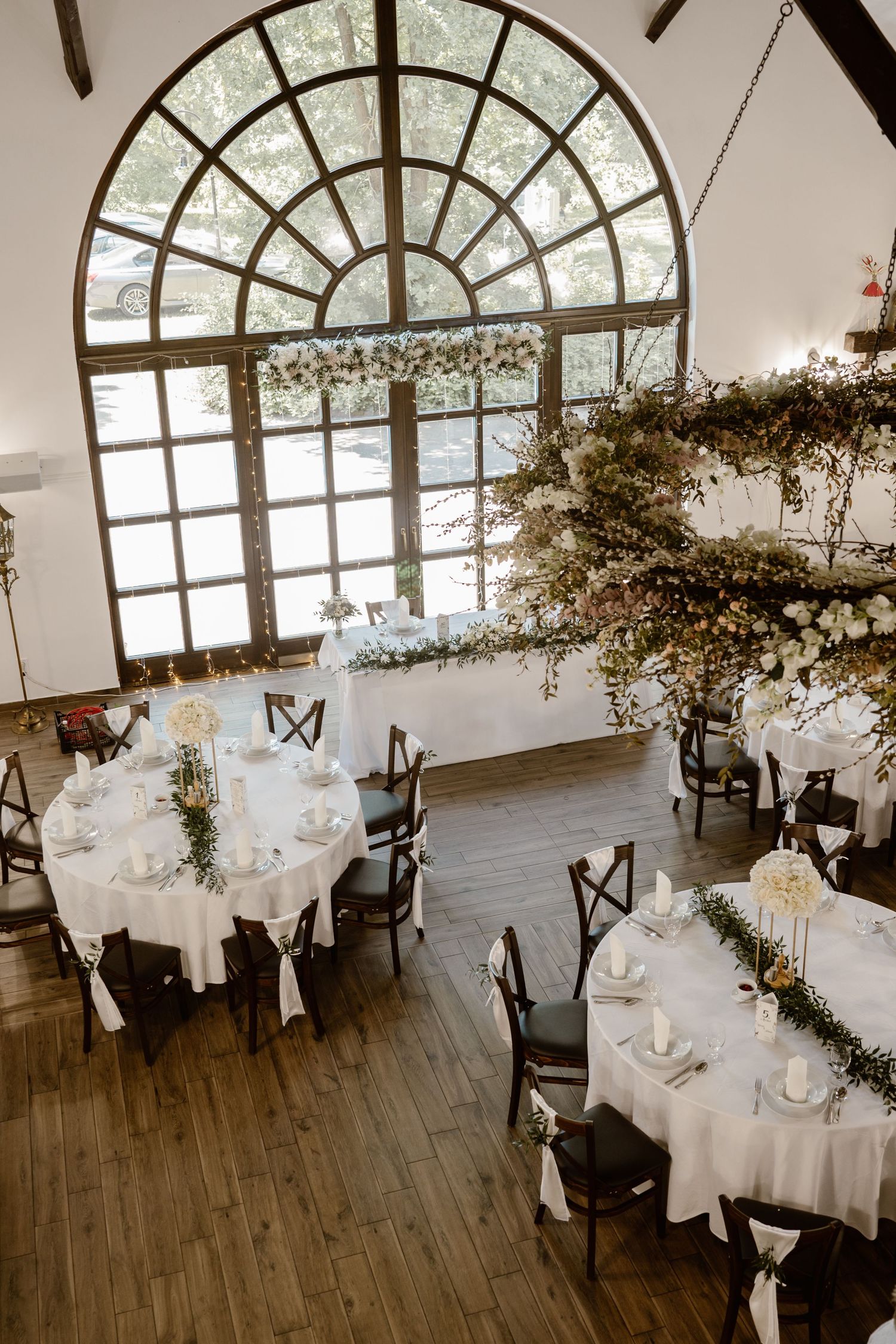 Elegant wedding reception venue with arched windows and white table settings decorated with floral arrangements.