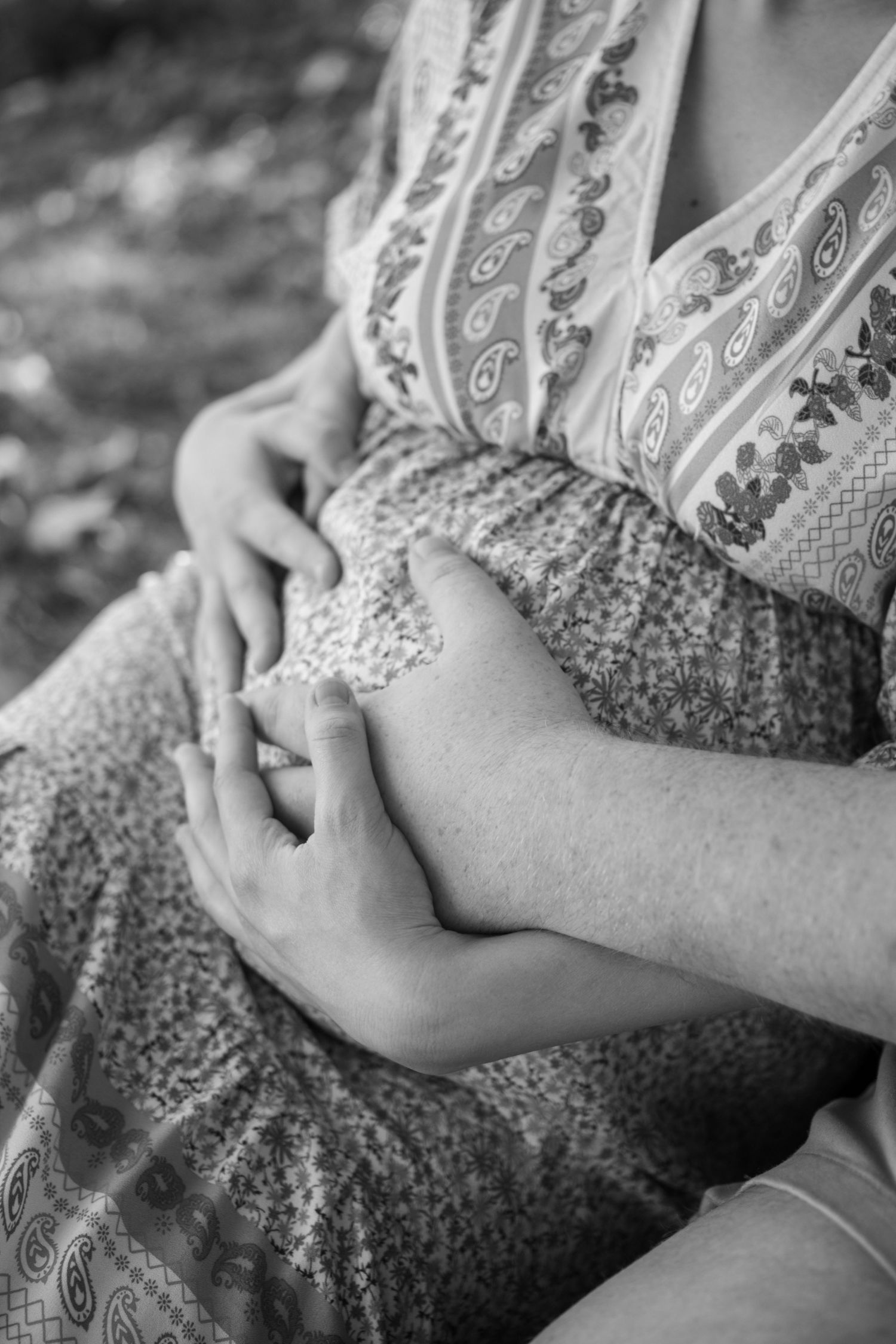 A black and white close-up of hands cradling a pregnant belly in a patterned dress.