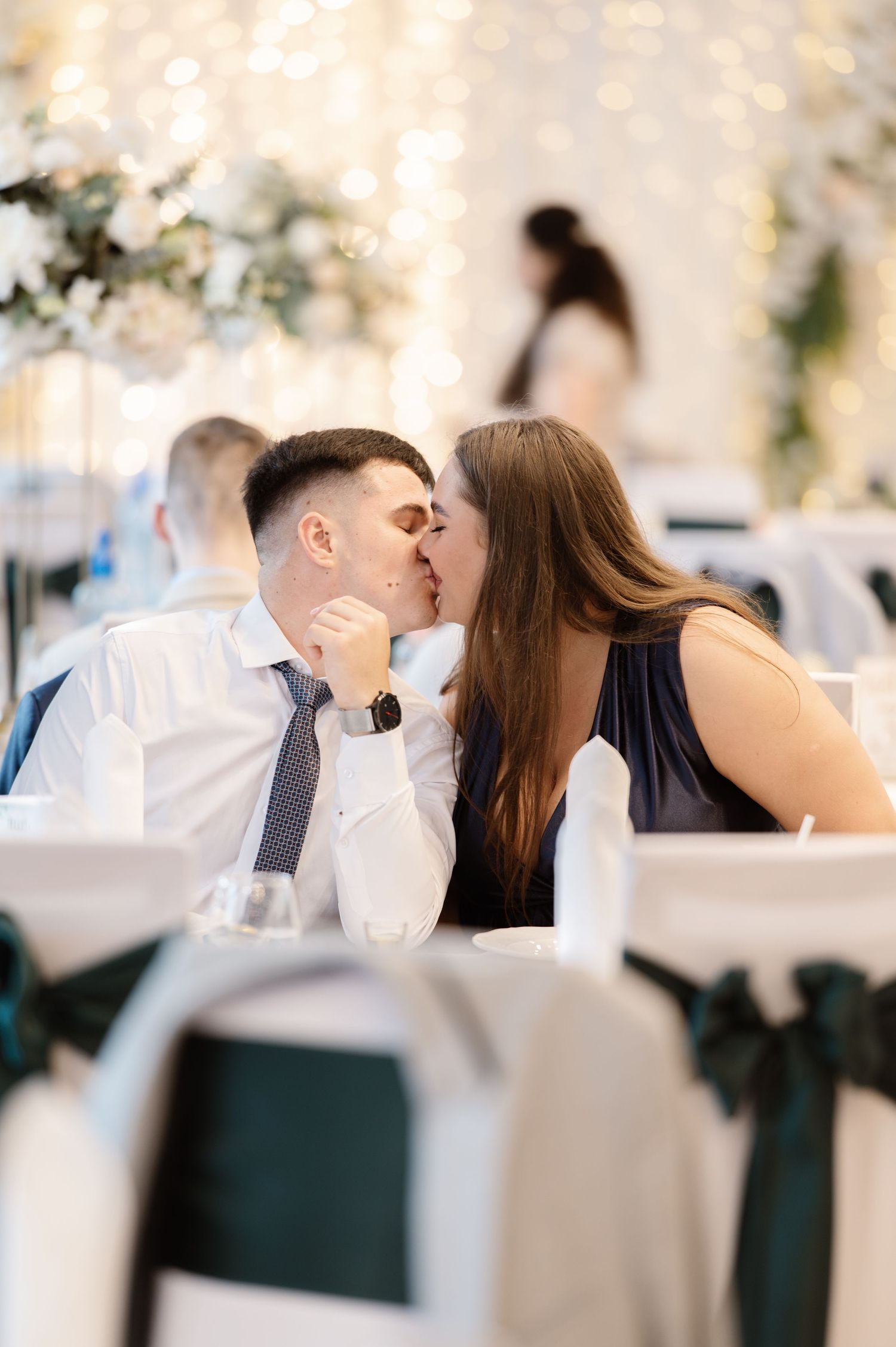 Romantic couple shares intimate moments at an elegant wedding reception with bokeh lights.