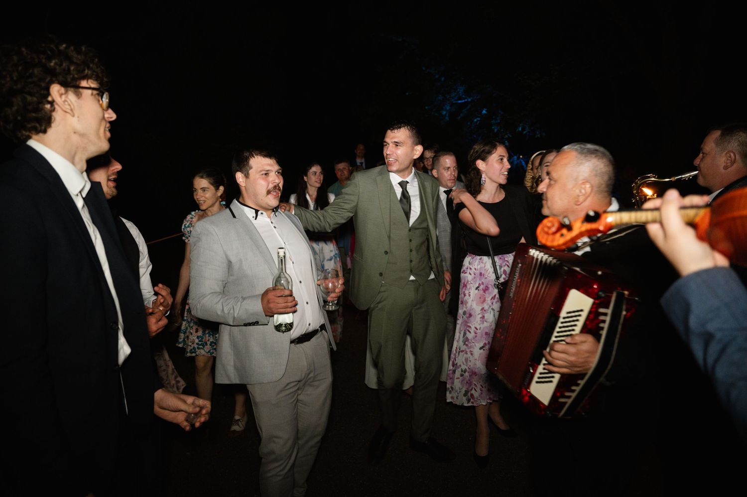 Musicians perform at a dimly lit wedding reception with guests dancing.