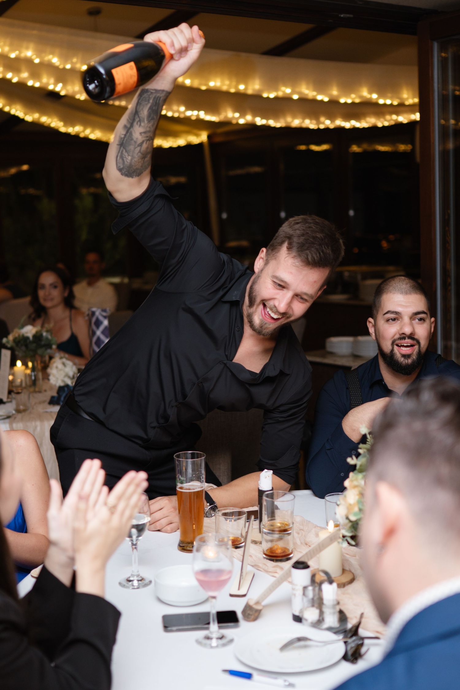 Wedding reception guests celebrating enthusiastically at decorated dining tables.