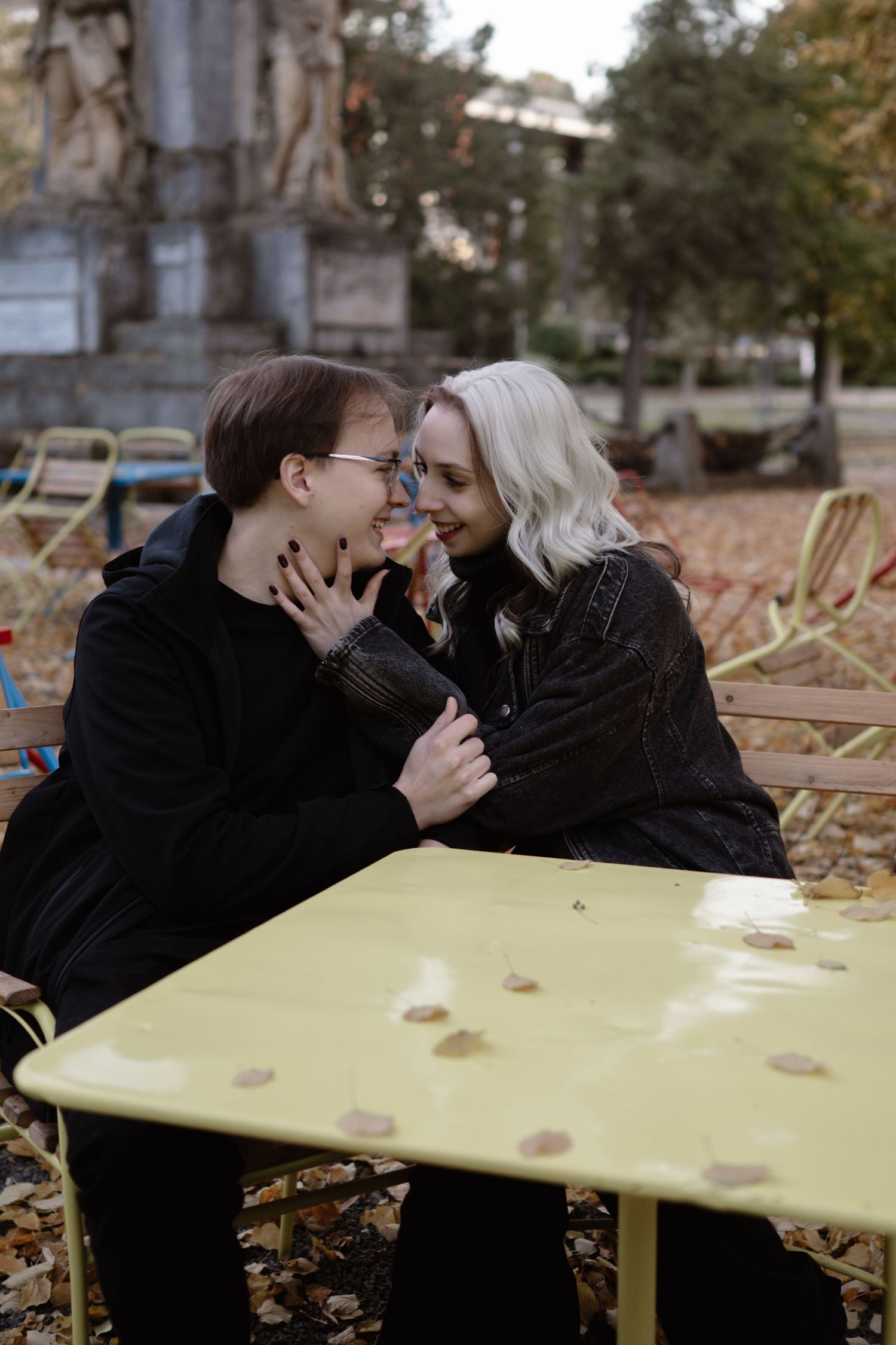 Couple shares tender moment at yellow table surrounded by autumn leaves.